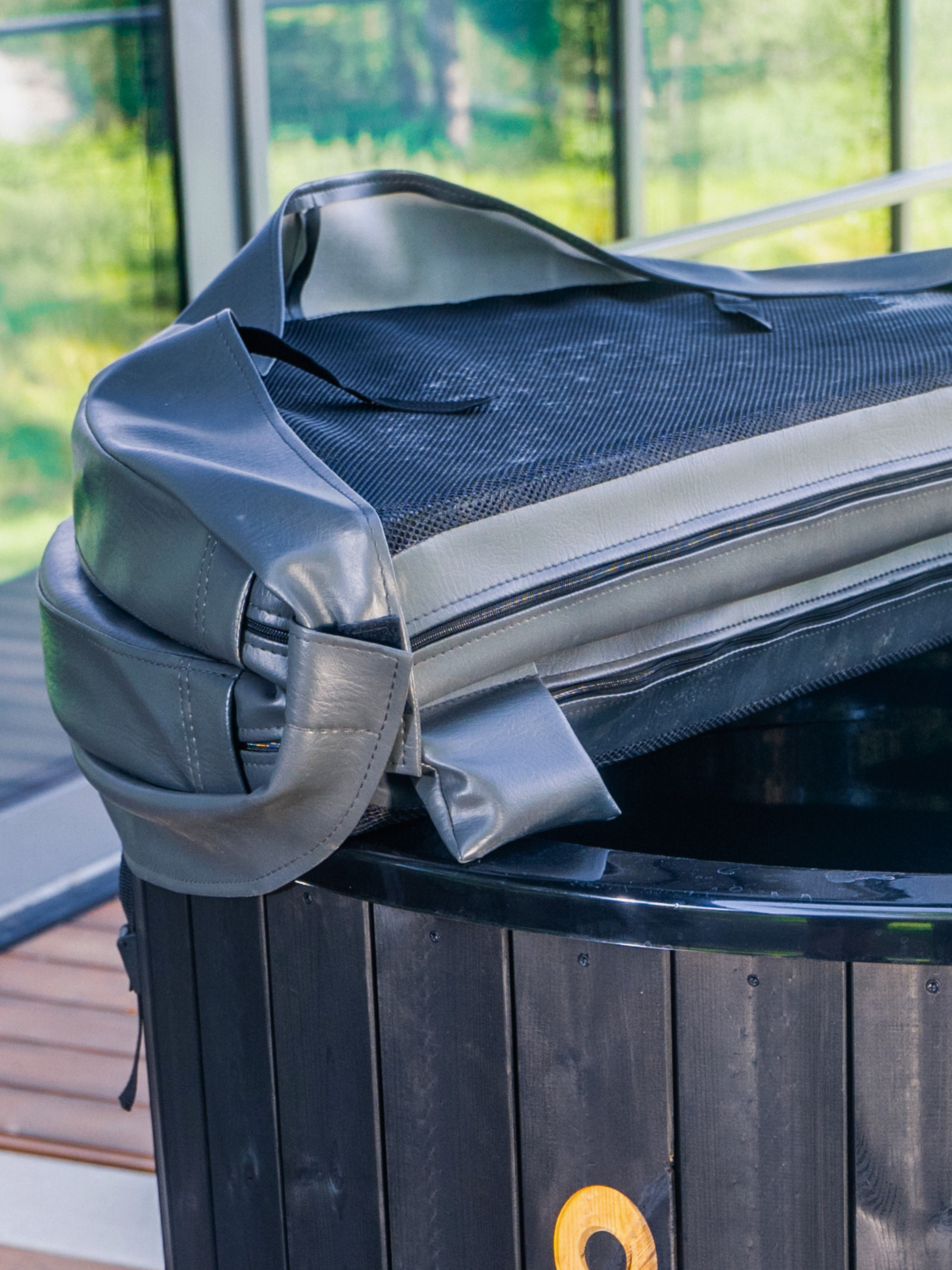 Black trash bin with a gray liner partially pulled up, showing a wooden deck and greenery in the background.