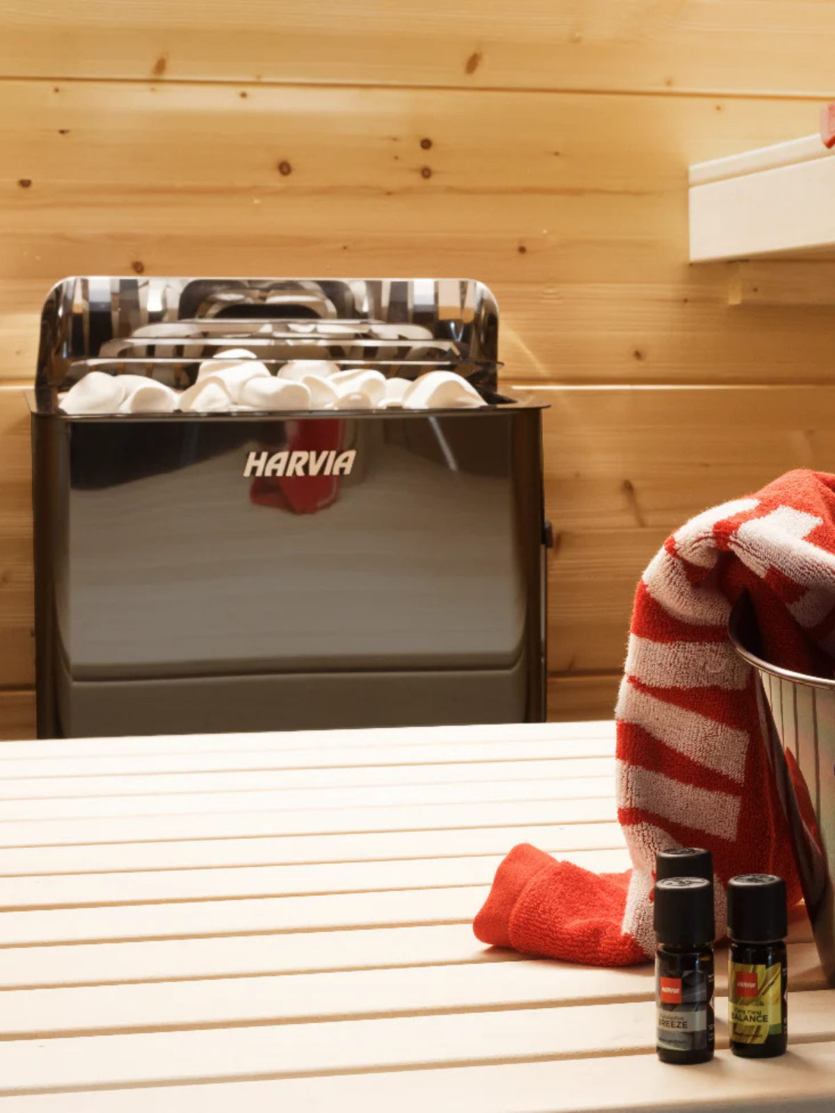 Harvia sauna heater in a wooden sauna with towels and bottles on a bench.