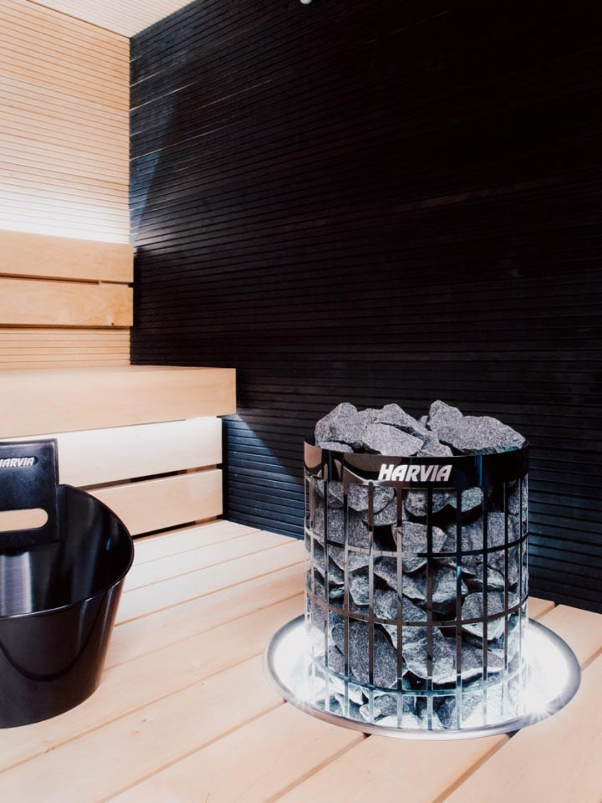 Harvia sauna with wooden interior and black wall, featuring a basket of stones.