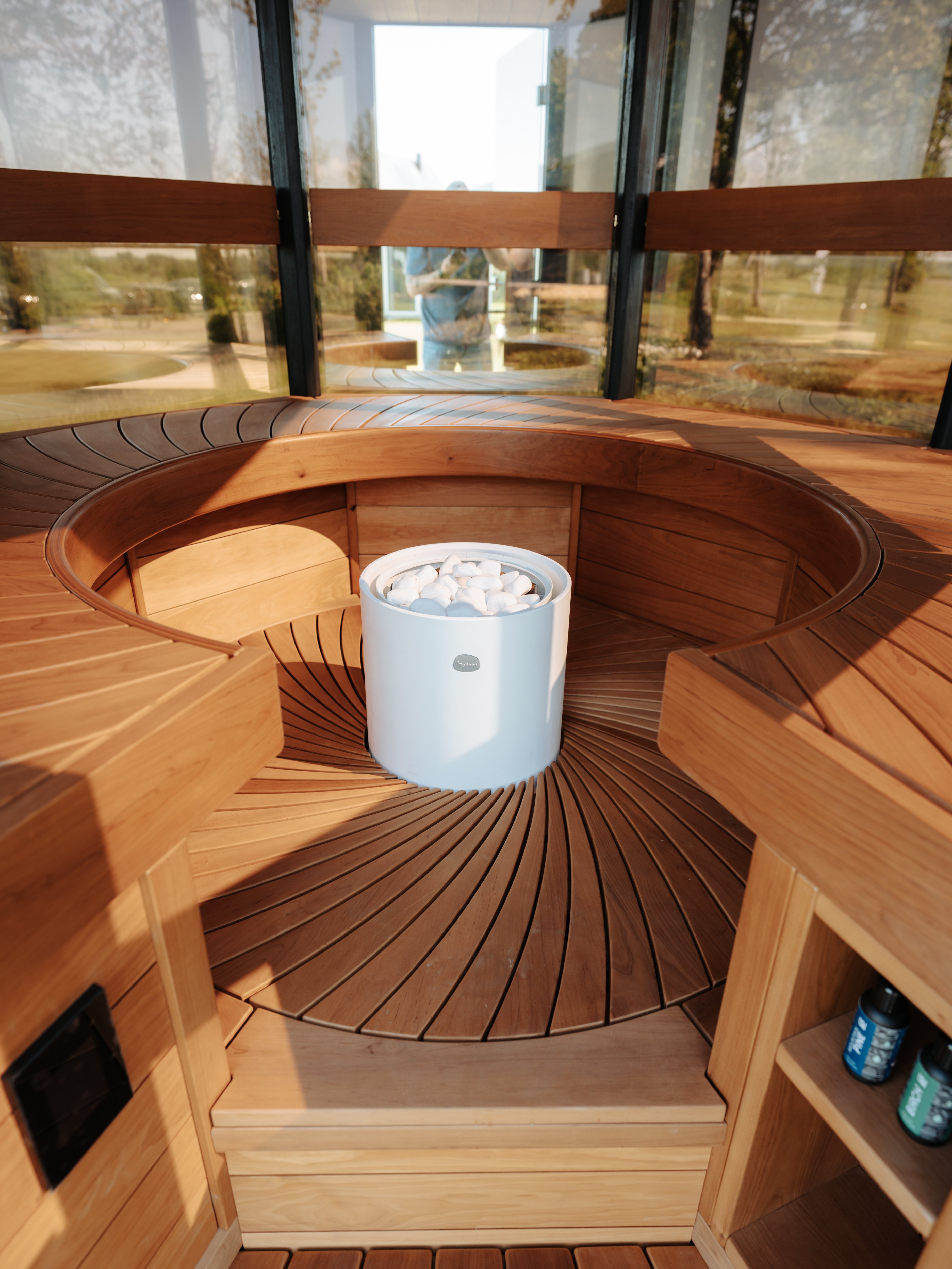 Wooden sauna with a circular bench and a white bucket of stones inside