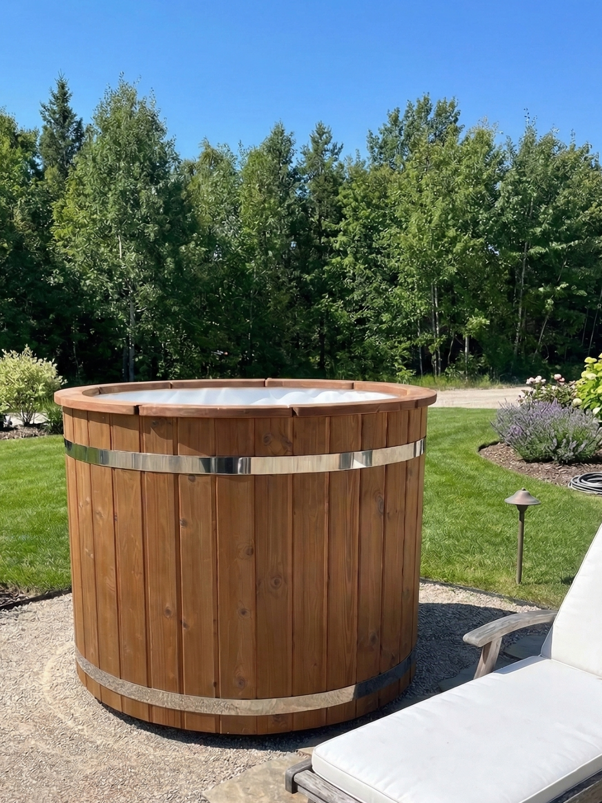Wooden hot tub in a backyard setting with trees and grass.