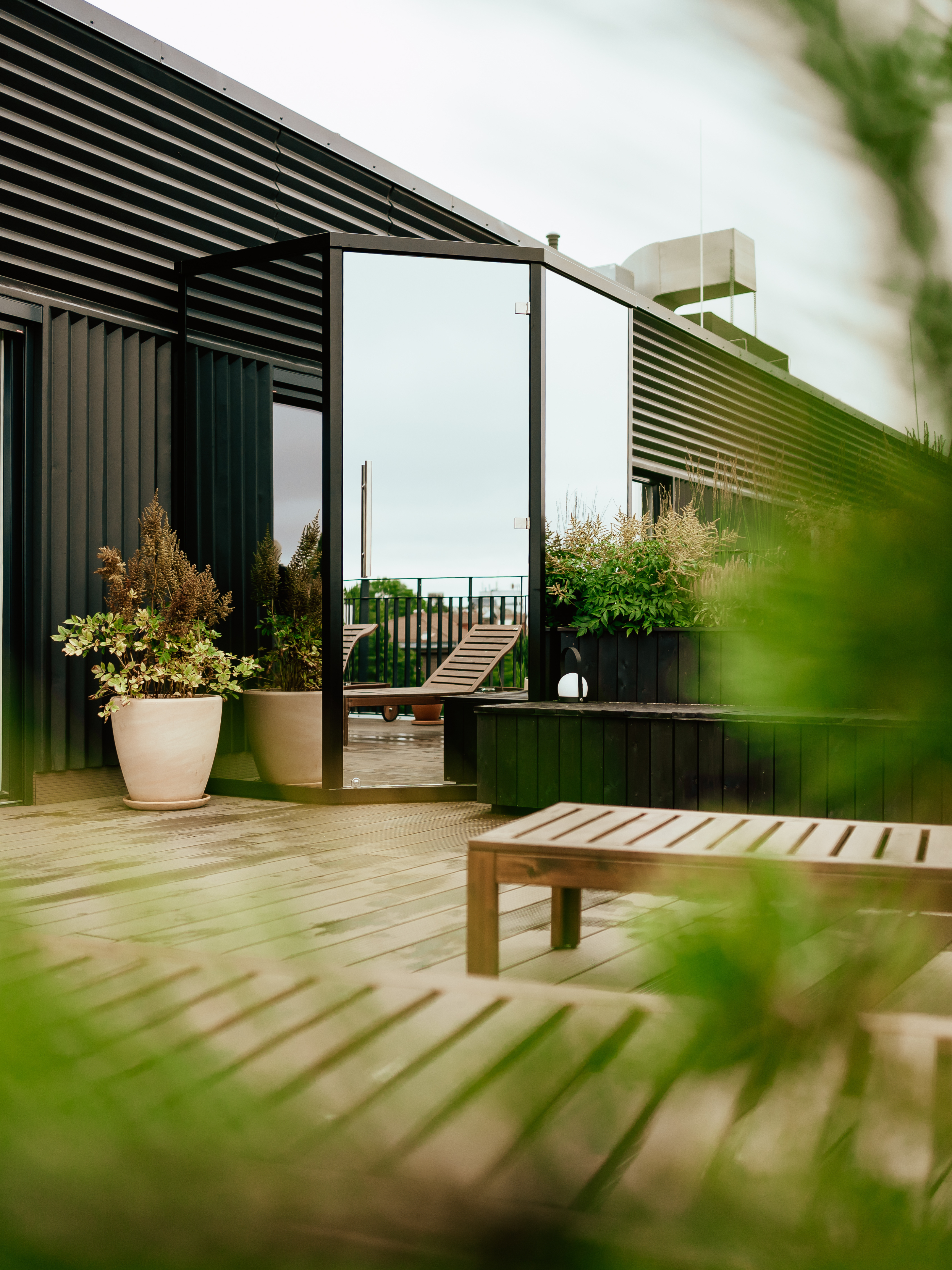 Outdoor patio area with wooden bench, potted plants, and modern building in the background.