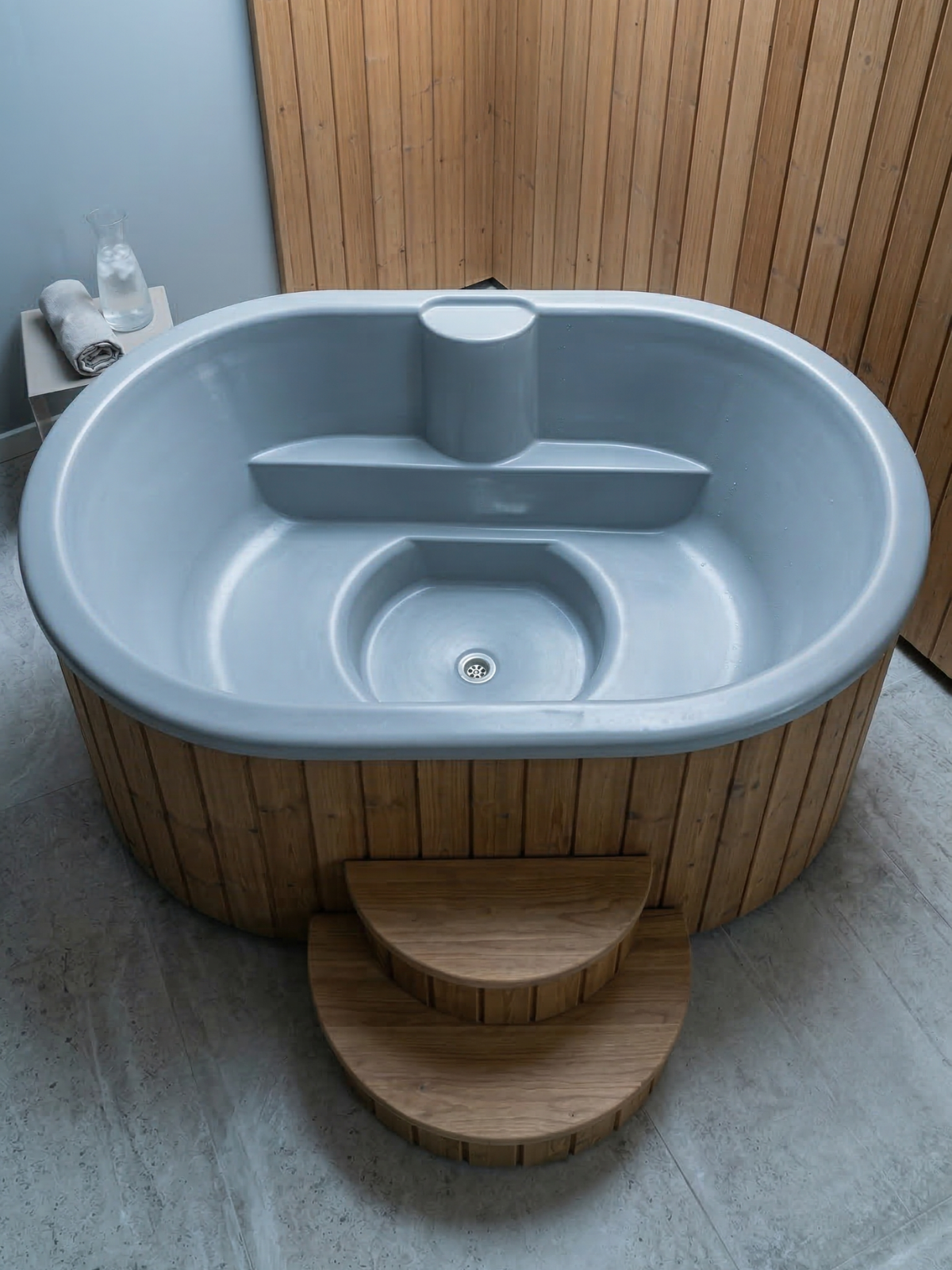 Gray hot tub with wooden steps in a bathroom setting