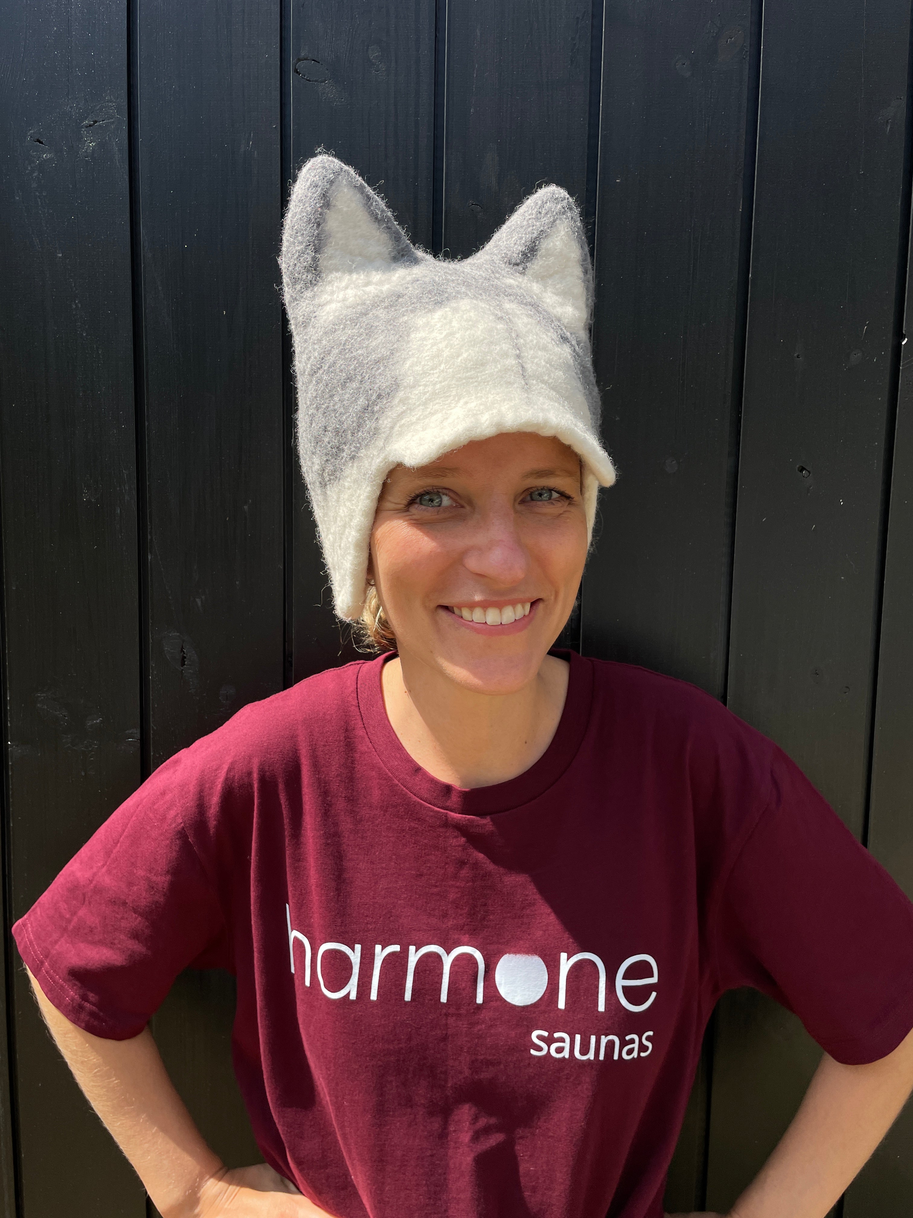 Person wearing a maroon shirt with 'Harmone Saunas' logo and a white knit hat on a dark wooden floor.