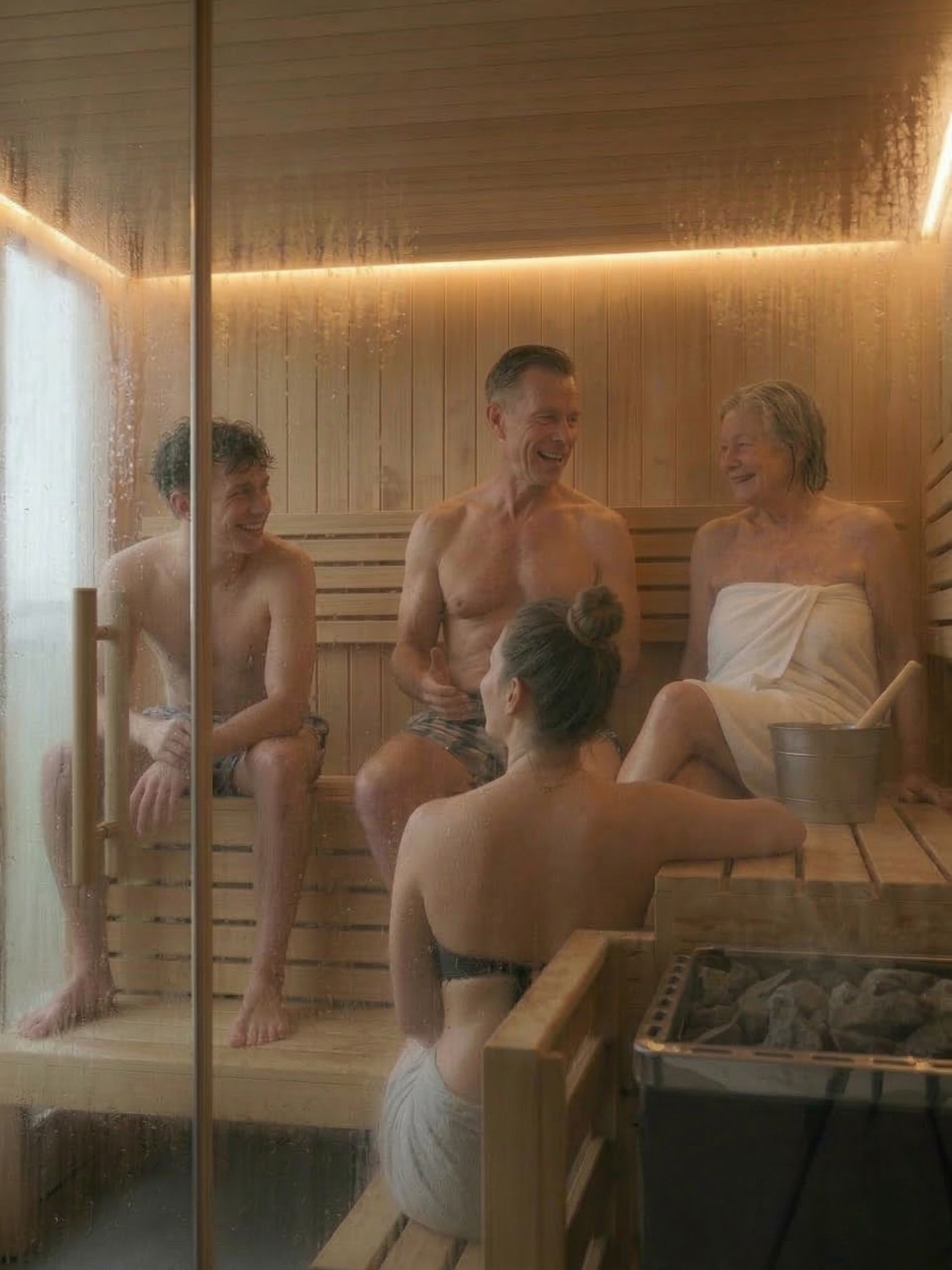 People in a sauna with wooden walls and a glass door.