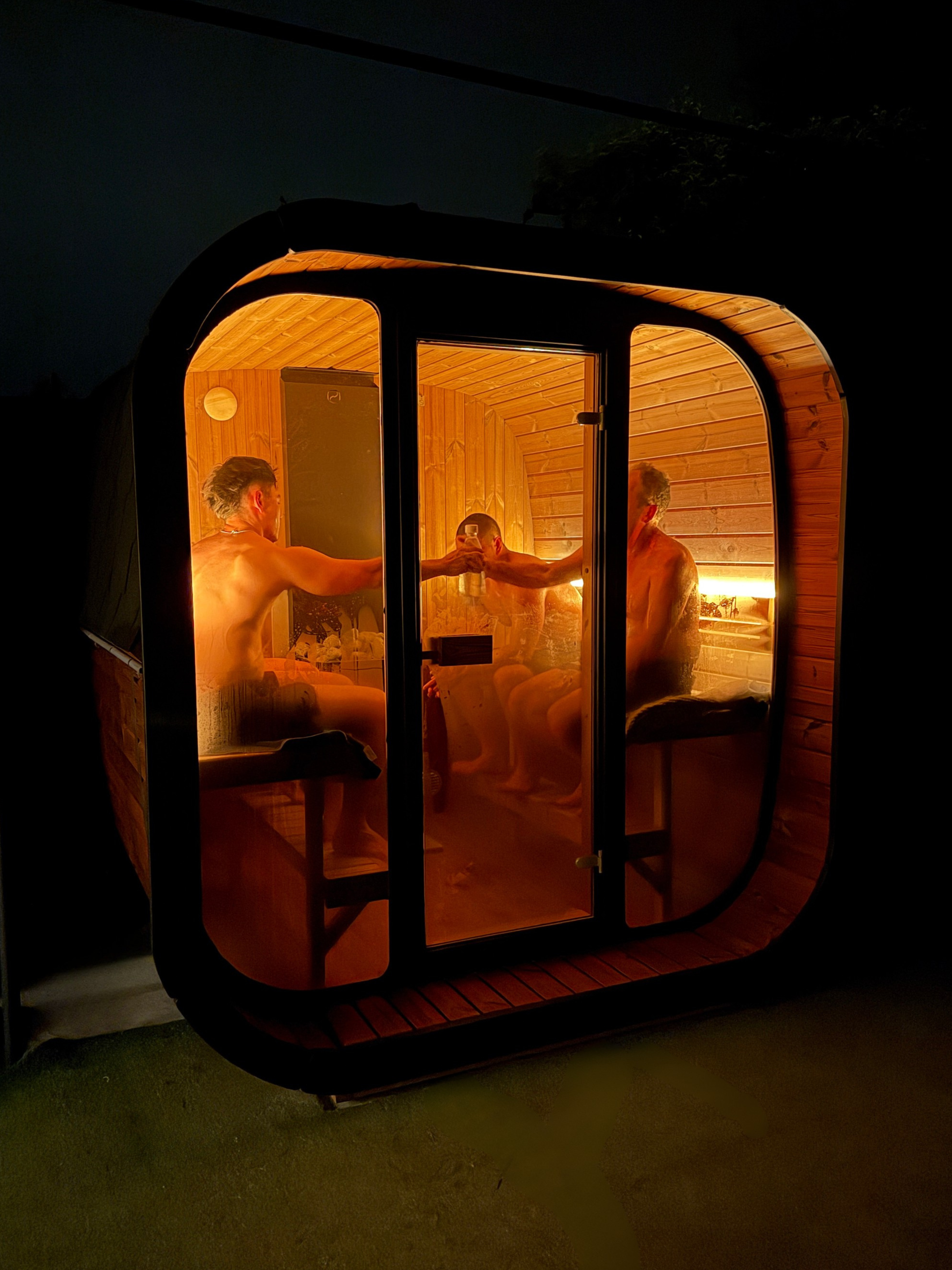 Two people in a small, enclosed sauna-like room with warm lighting.