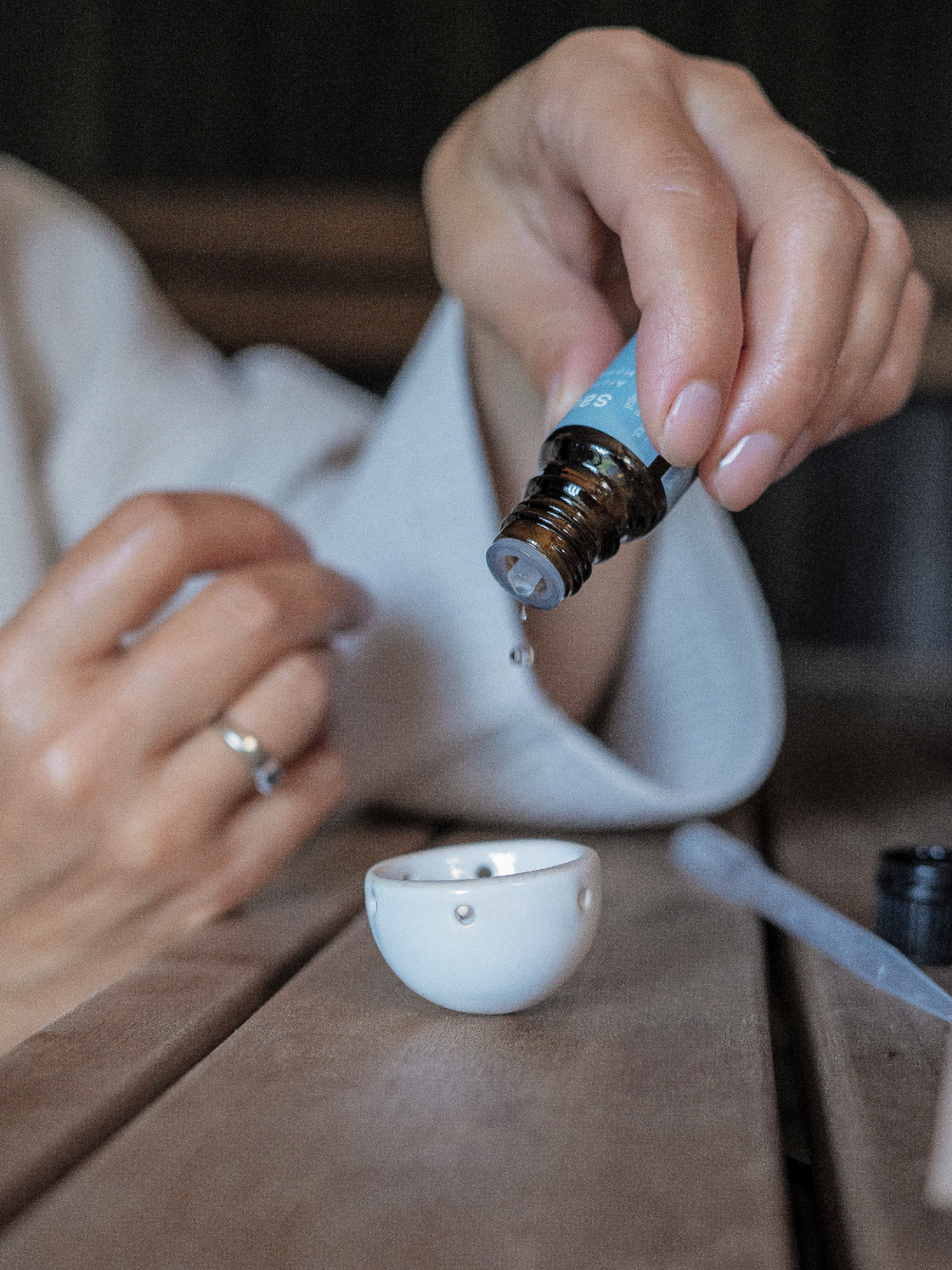 Person using a dropper to add liquid from a small bottle into a white cup on a wooden surface.