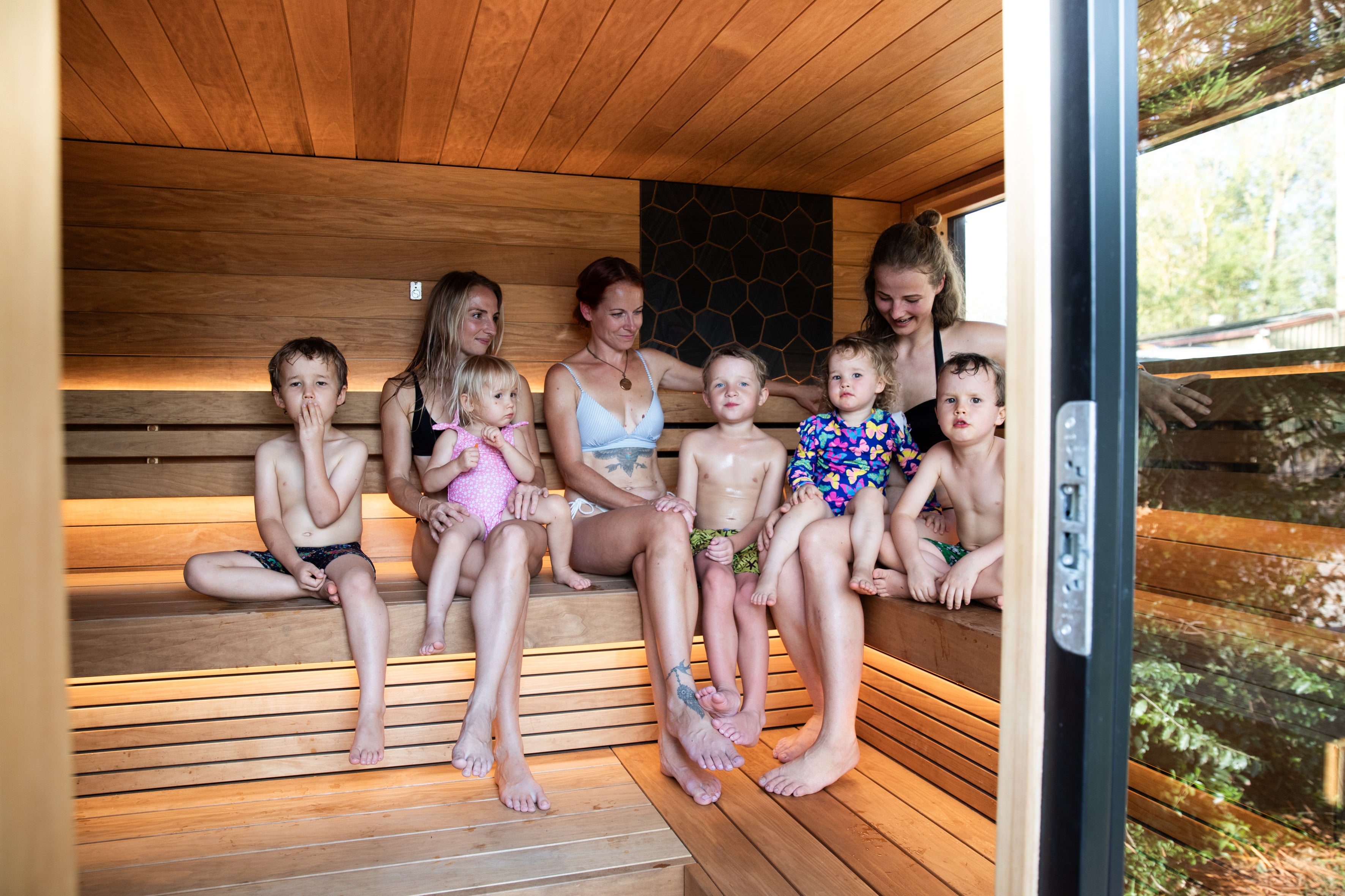 Group of people, including children, sitting inside a wooden sauna.