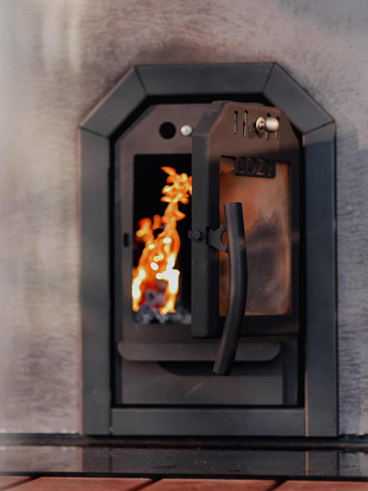 Wood-burning stove with flames inside, mounted on a stone wall.