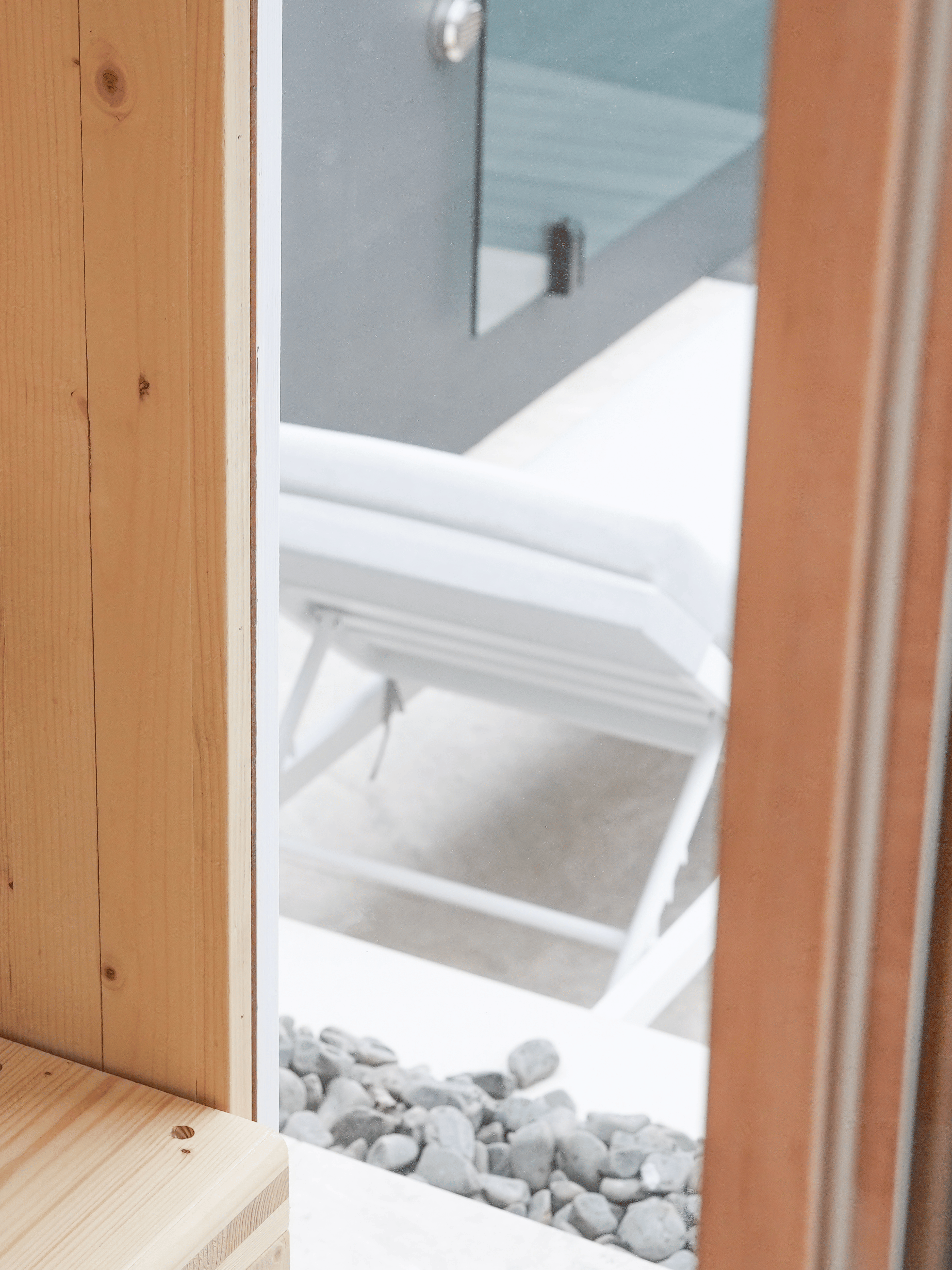 Wooden door partially open with a view of pebbles and a white structure outside.