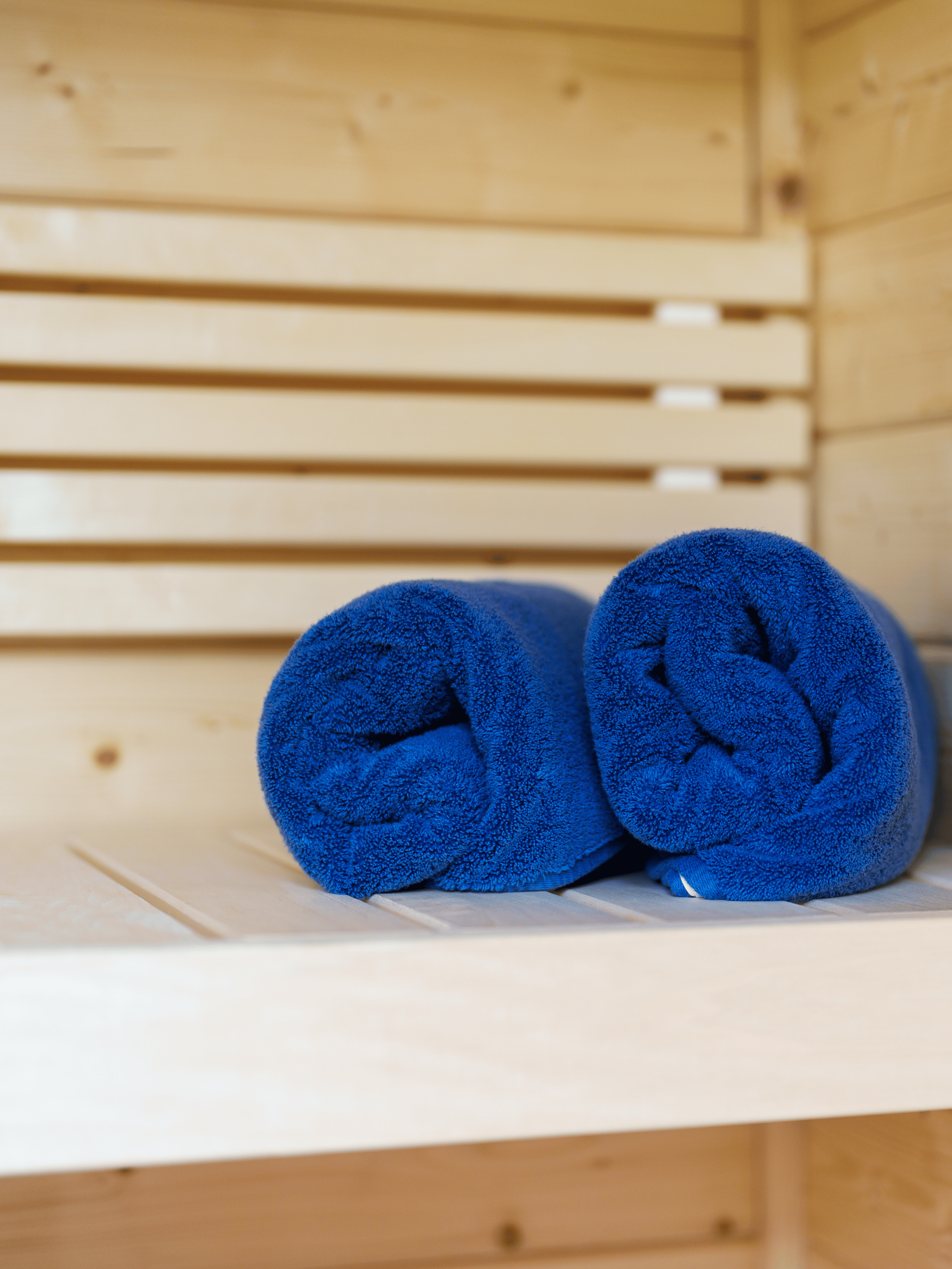 Two blue towels rolled up on a wooden bench in a sauna.