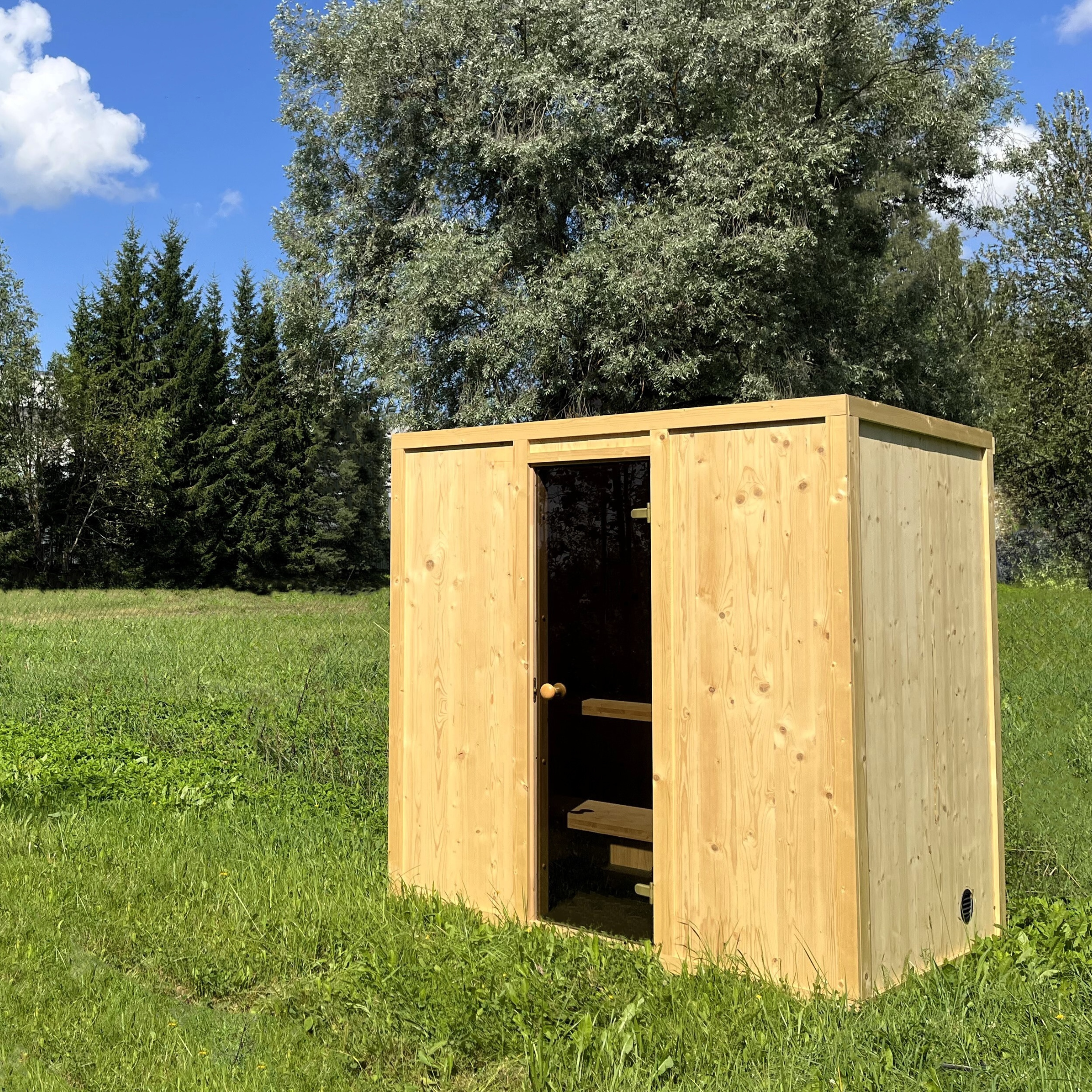 Wooden shed in a grassy area with trees in the background