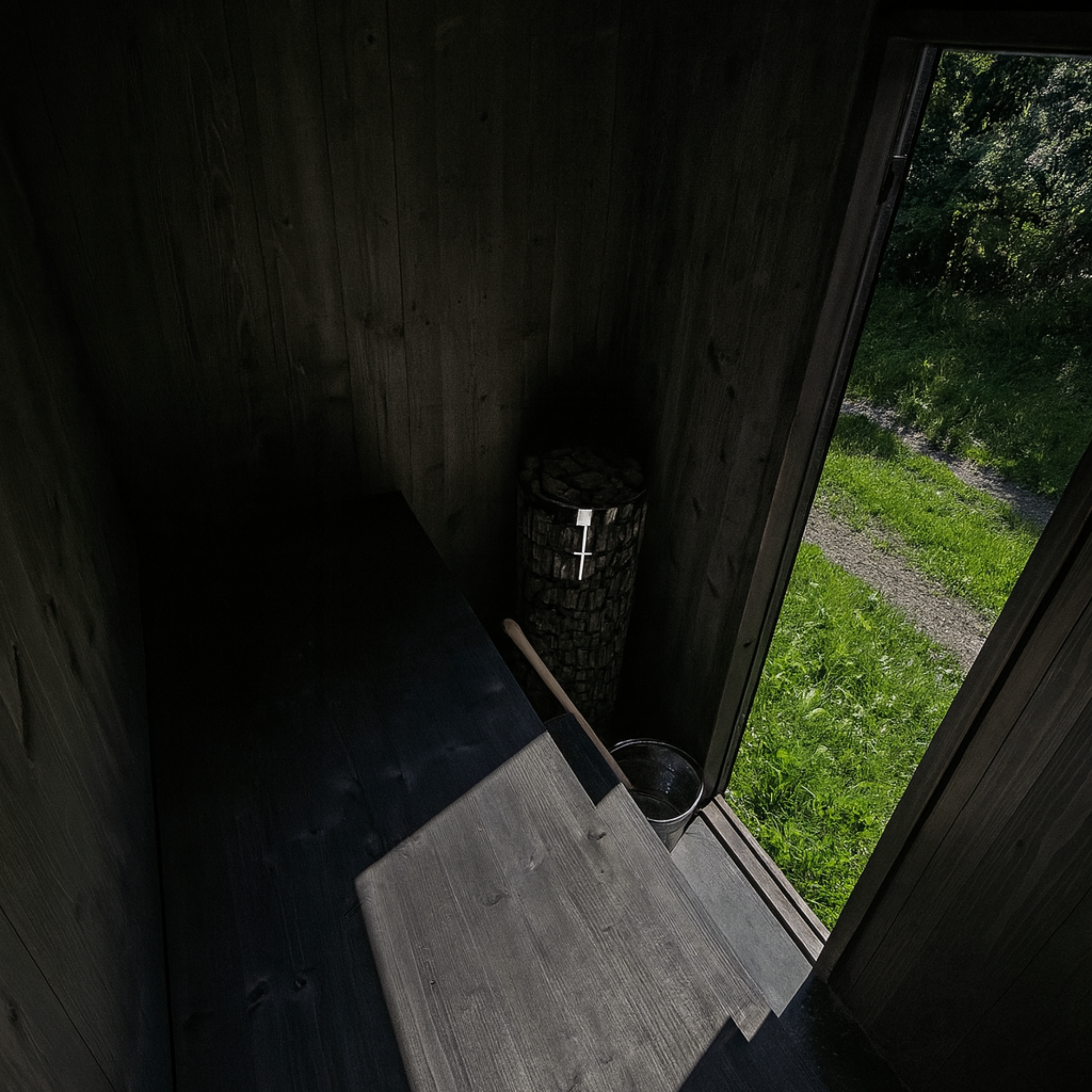 Wooden interior with a bucket and mat, leading to an outdoor grassy area.