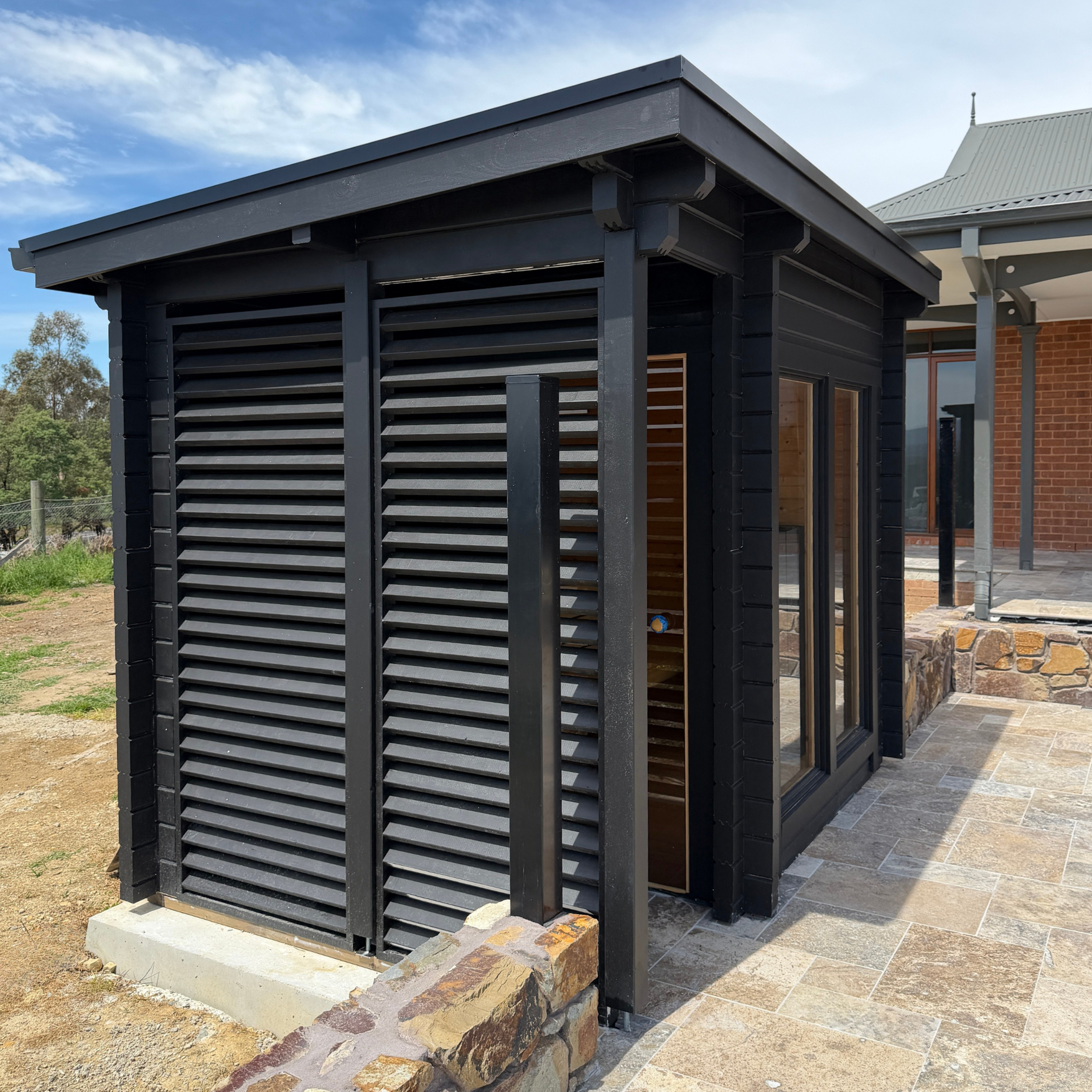 Modern outdoor shed with black exterior and wooden interior, set against a clear sky.