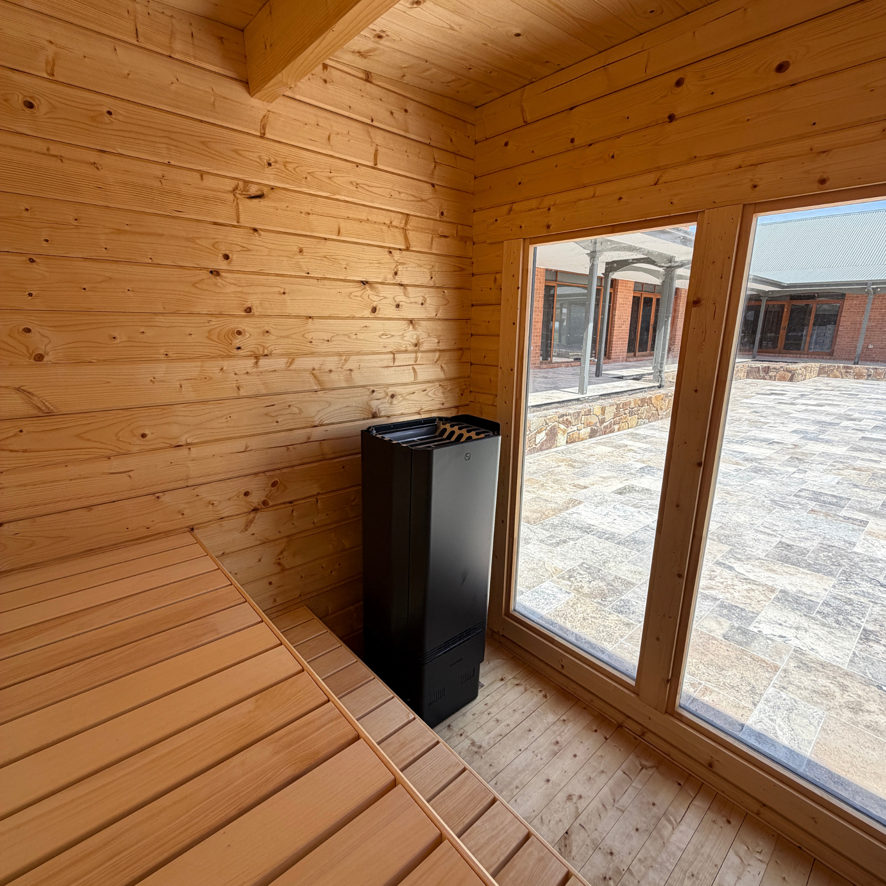 Wooden sauna interior with a black sauna heater and large windows.