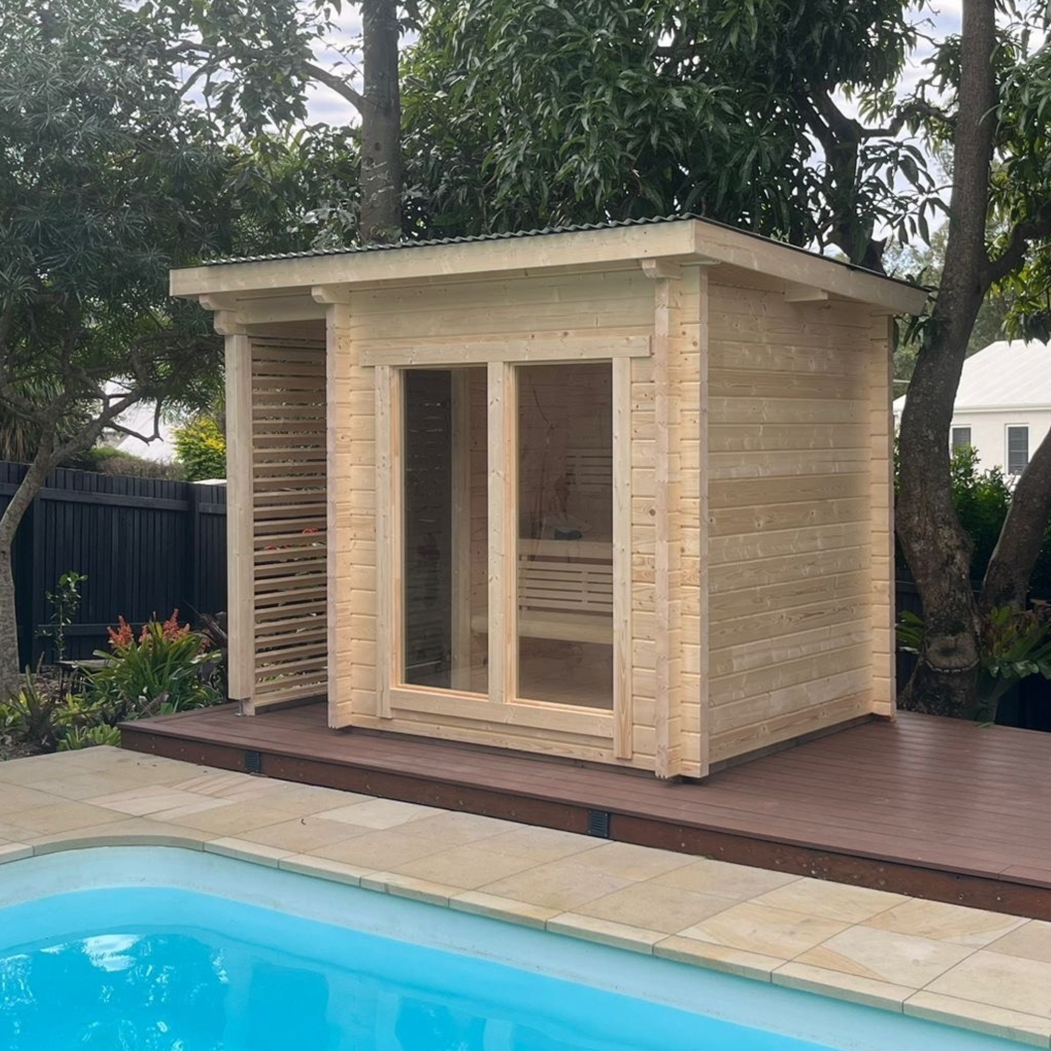 Wooden cabin attached to a poolside deck with trees in the background