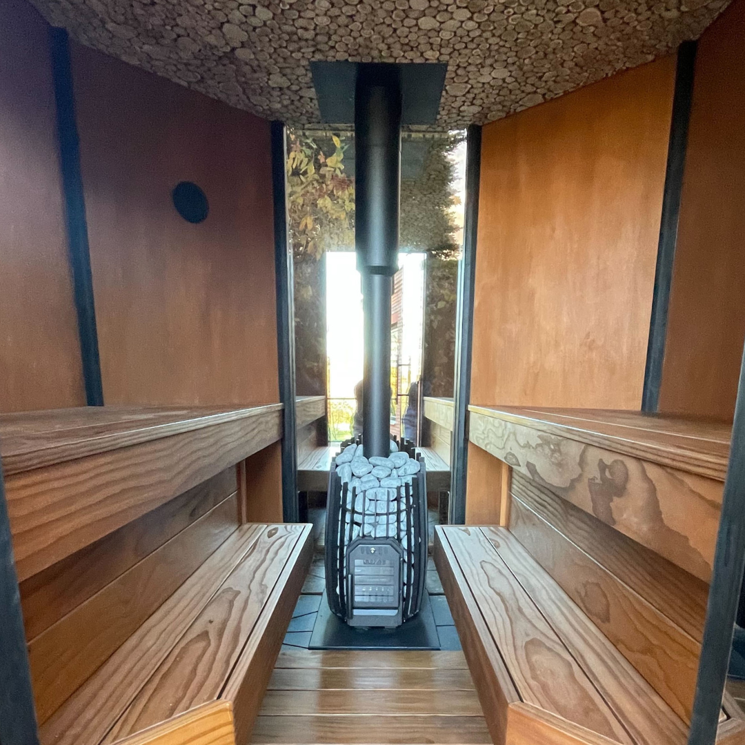 Wood-fired stove in a wooden sauna with benches on either side.
