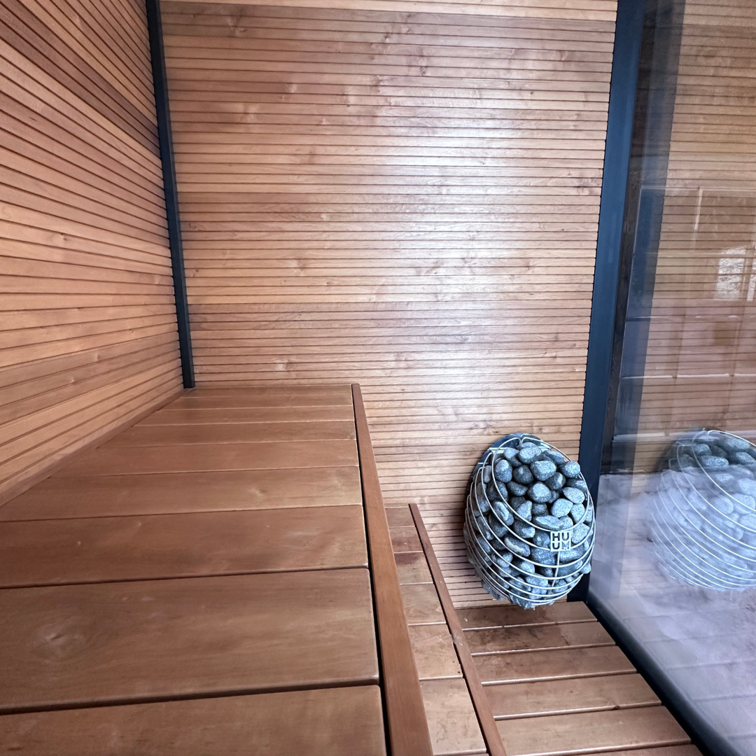 Wood-paneled sauna room featuring a bench and a modern stone heater, creating a warm, cozy, and relaxing atmosphere.