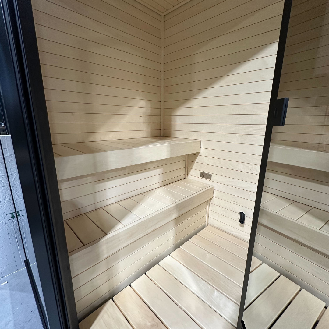 Modern wooden sauna interior with light-colored wood panels and benches. The design is minimalist and clean, creating a calm and inviting atmosphere.