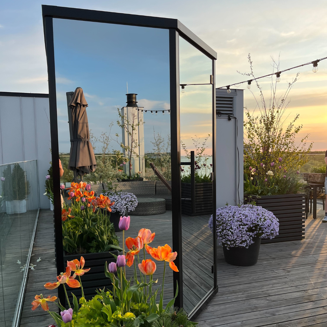 Rooftop patio at sunset with vibrant orange and purple tulips reflected in a tall mirror. String lights and potted plants create a serene ambiance.