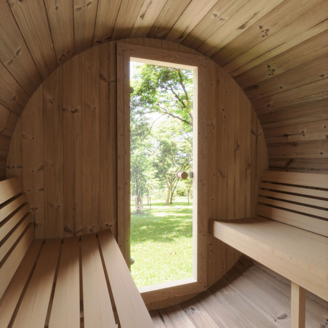 Interior of a wooden barrel sauna with benches, looking out through a vertical window onto a sunlit garden with green grass and trees. Calm and serene atmosphere.