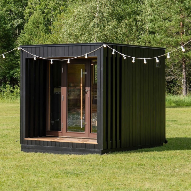 Portable cabin with black exterior and glass doors in a grassy outdoor setting.