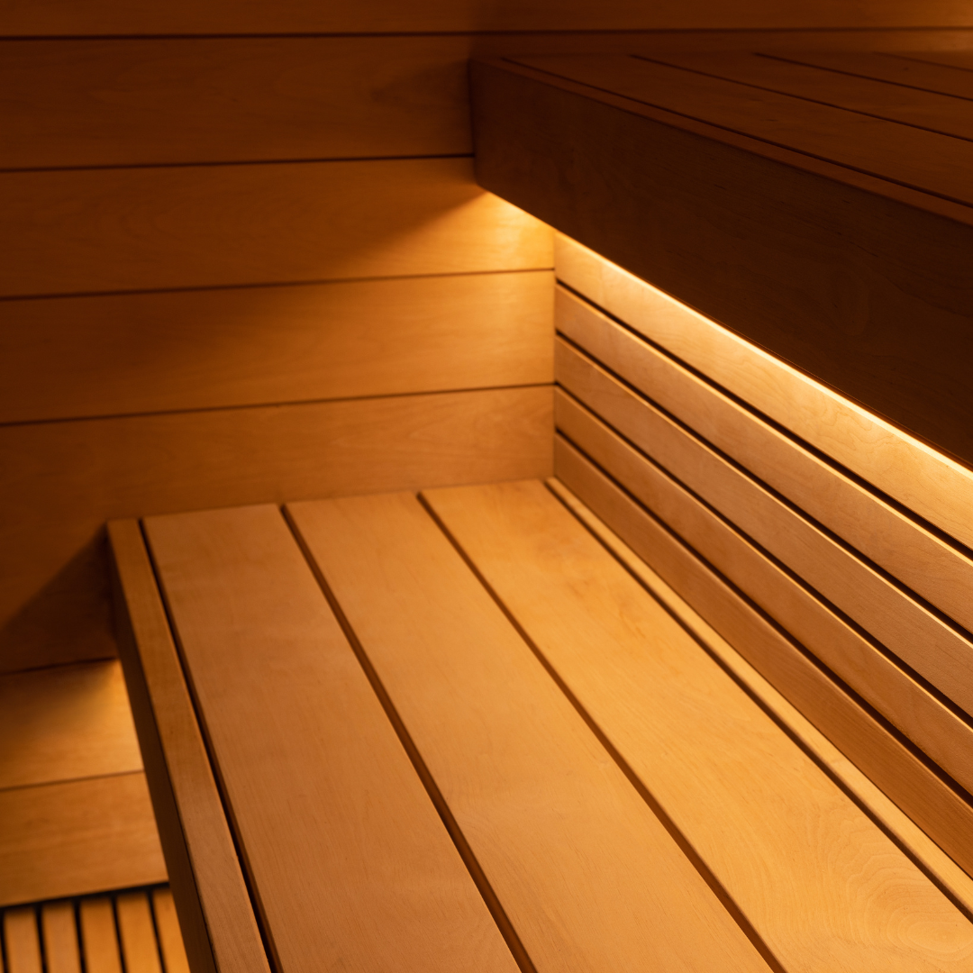 Wooden sauna interior with warm ambient lighting. The seating is made of smooth horizontal wooden planks, creating a serene and relaxing atmosphere.