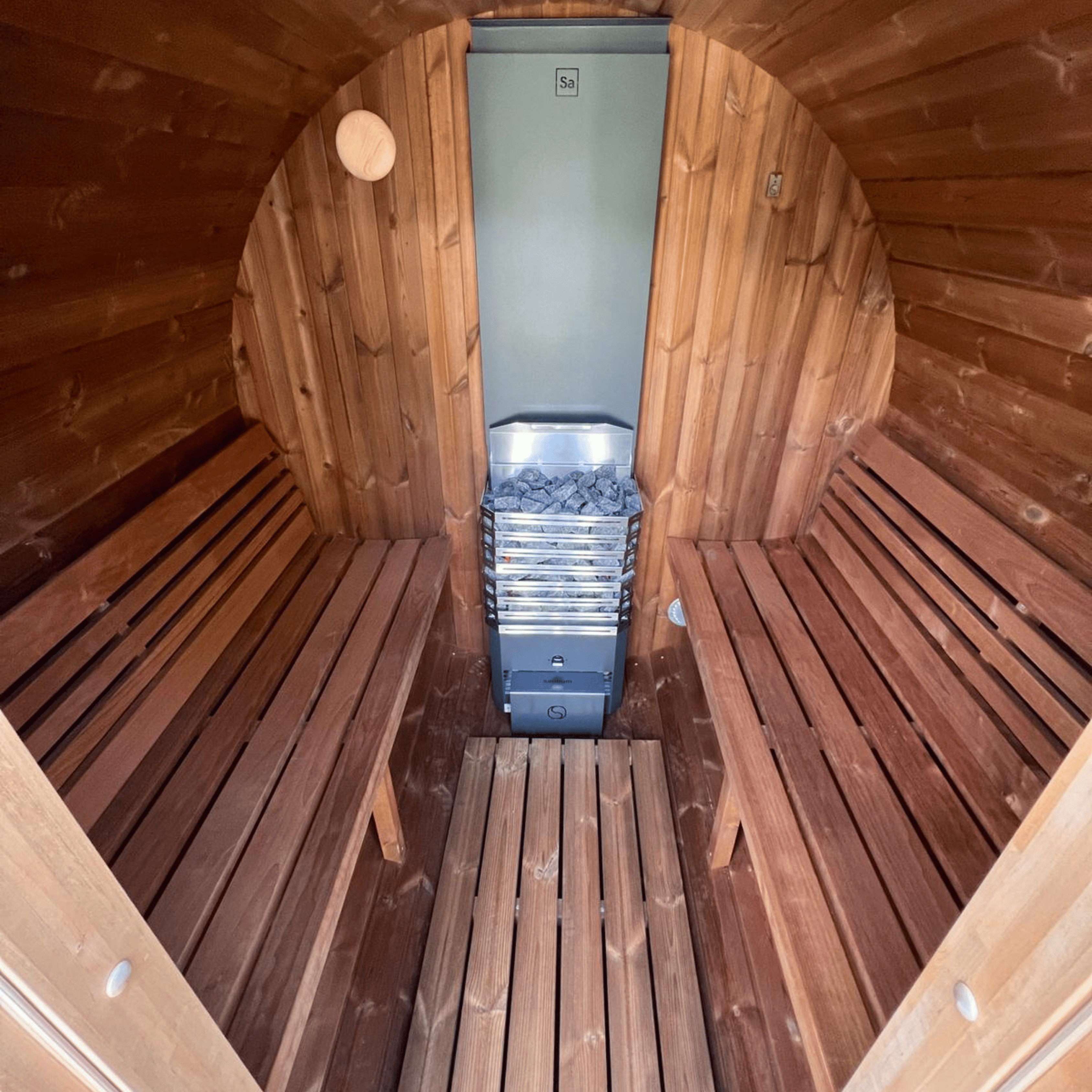 Wooden sauna interior with benches and a metal basket of stones.