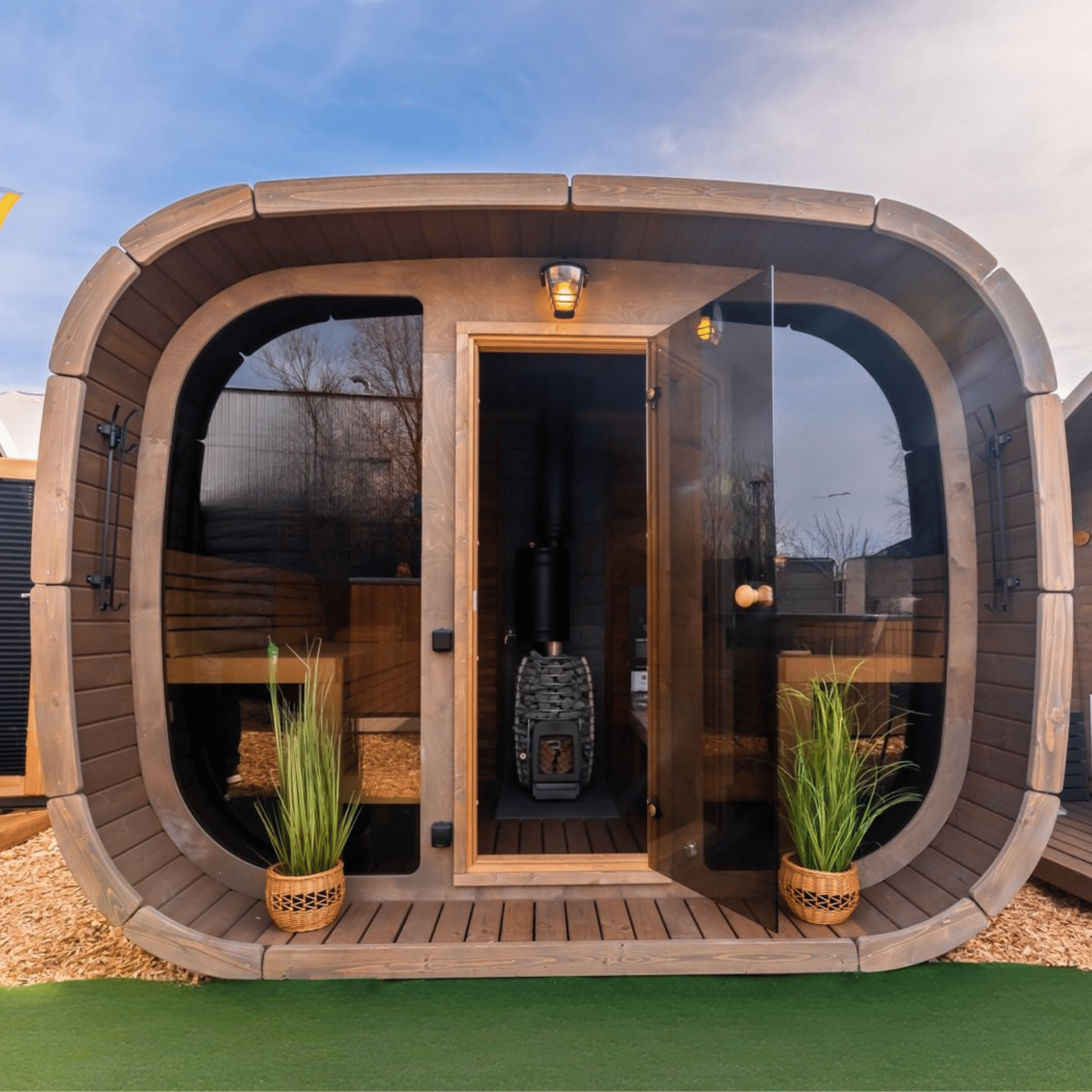Wooden outdoor pod with glass doors, plants, and a blue sky.