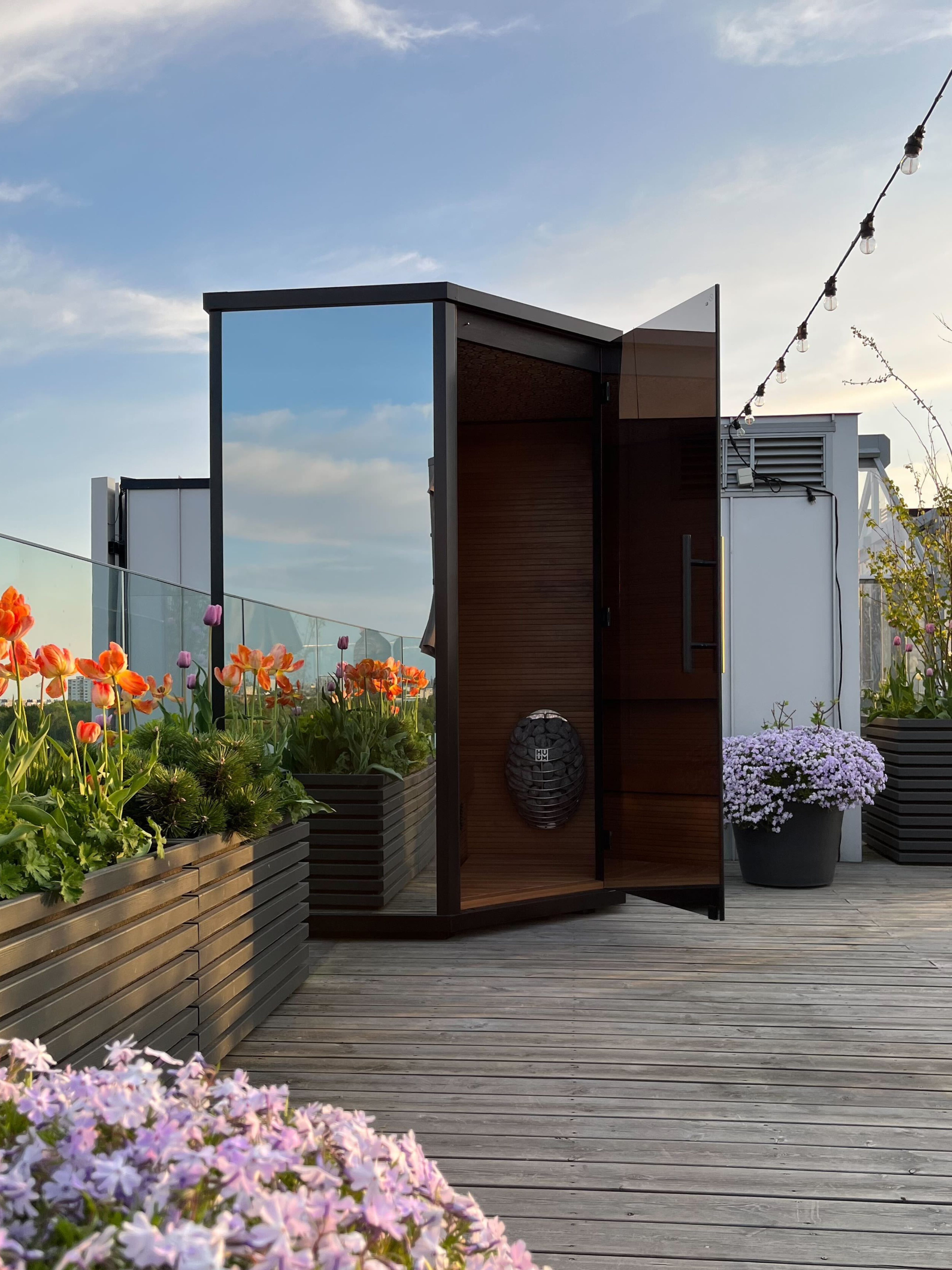 Modern outdoor shower cabin on a rooftop with flowers and sky view