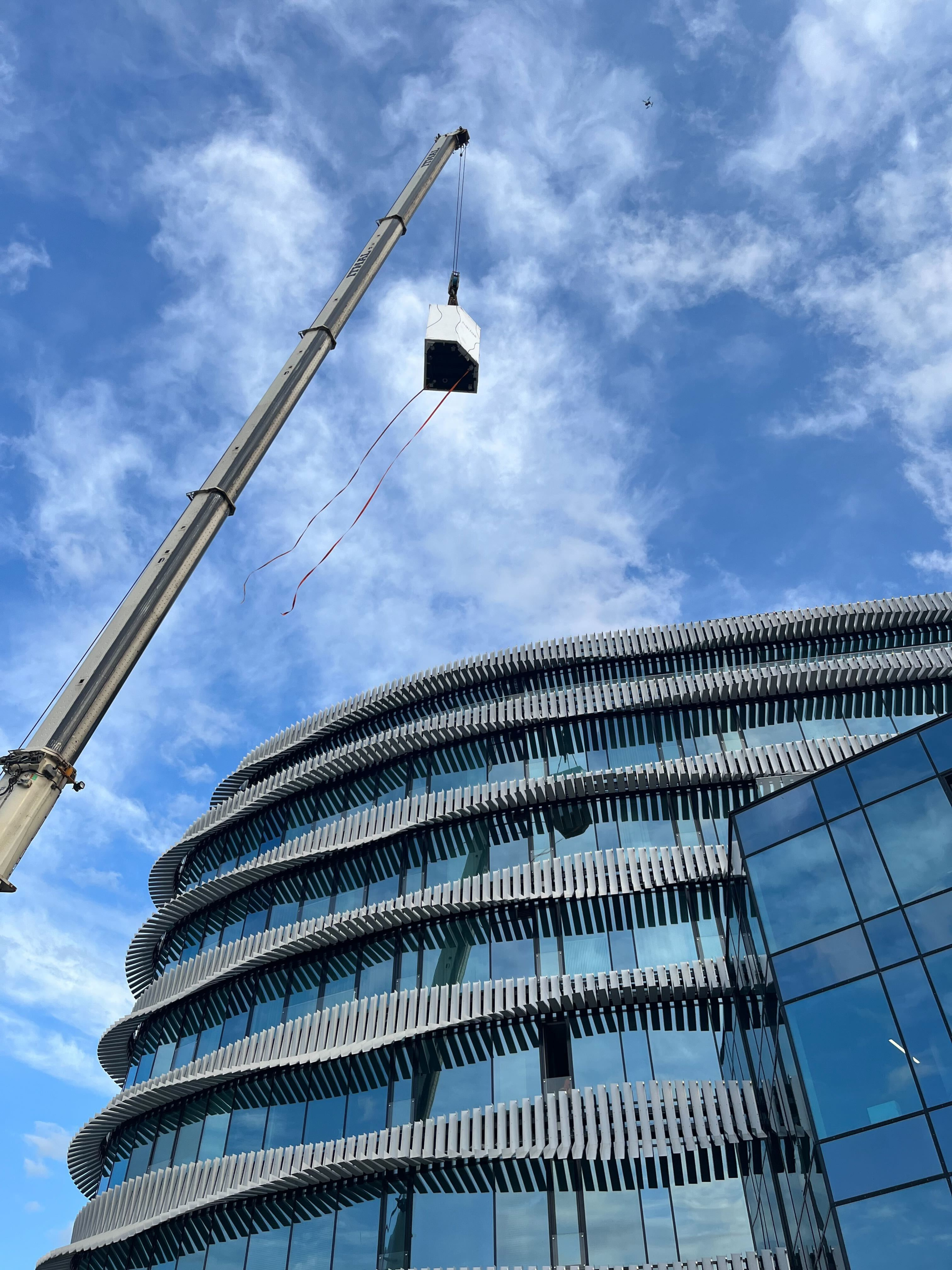 Crane lifting a load against a blue sky with clouds, near a modern building.