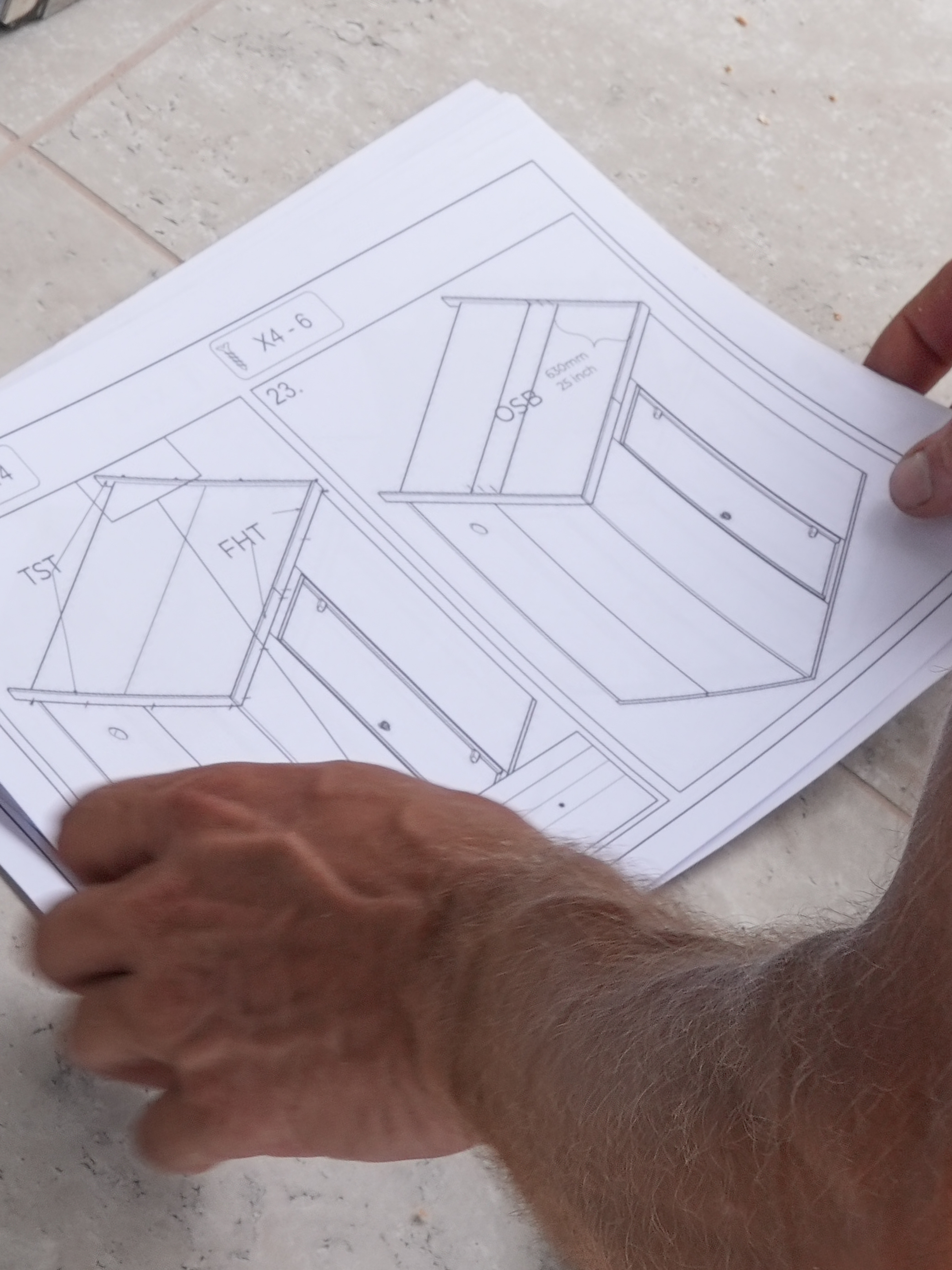 Hand holding a piece of paper with architectural drawings on a tiled floor.