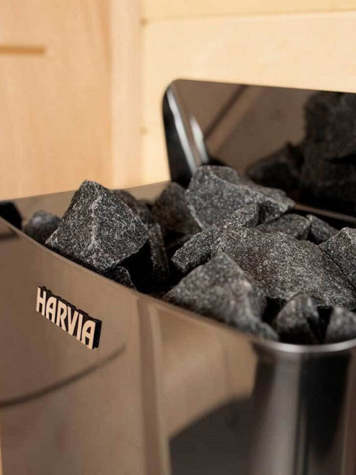 Harvia branded metal container with charcoal inside, set against a wooden background.