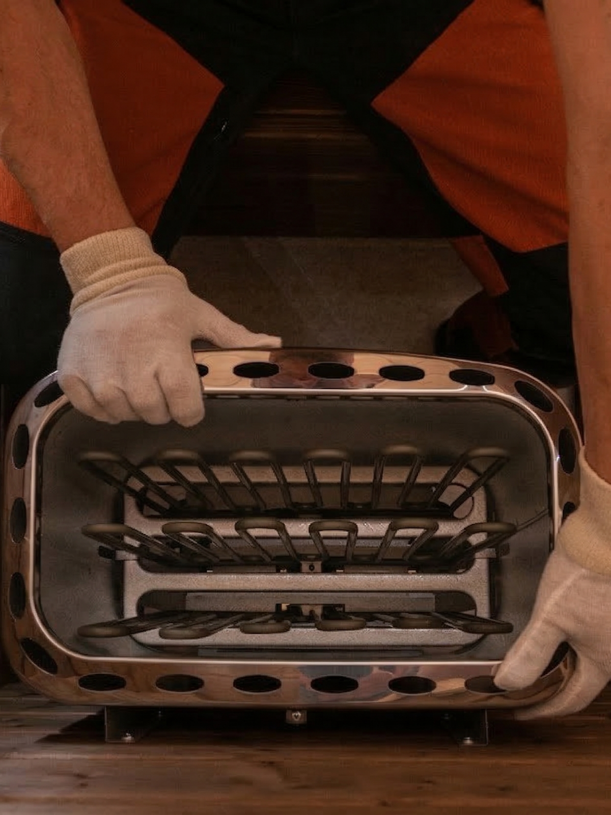 Person wearing gloves holding a metal grill basket with a wooden background