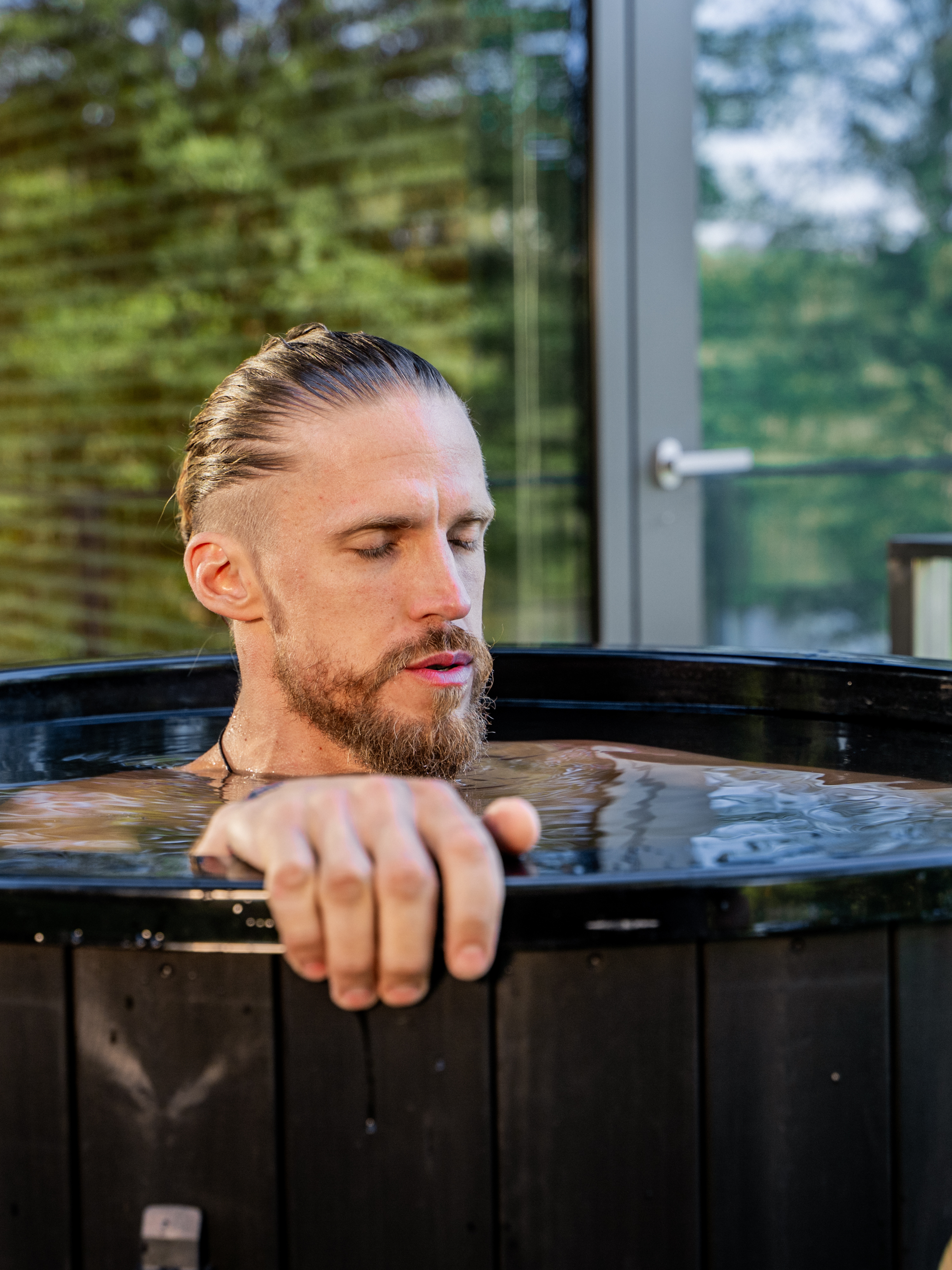 Man with a beard sitting in a hot tub with a blurred green outdoor background