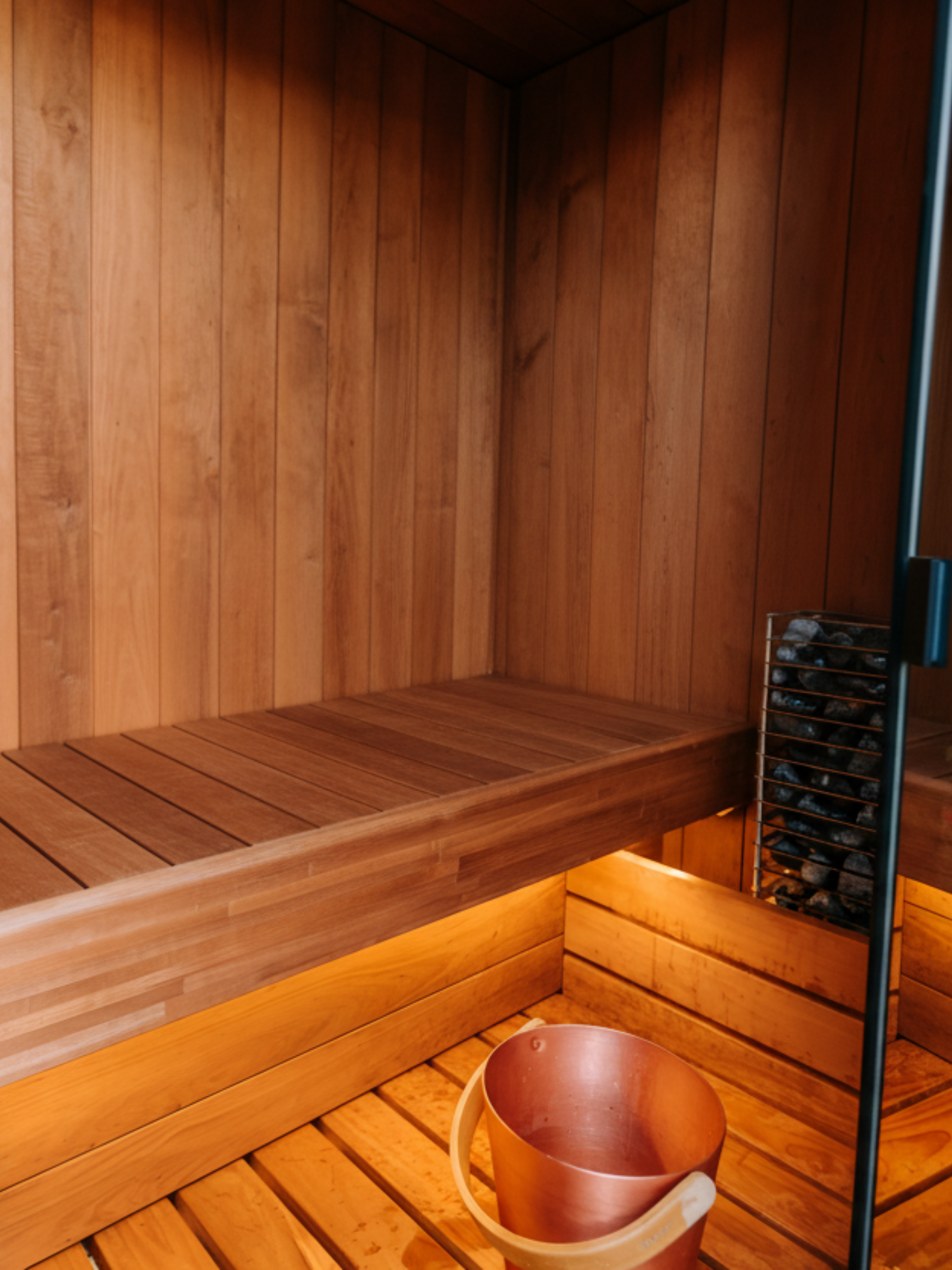 Wooden sauna with a wooden bench and a copper bucket.