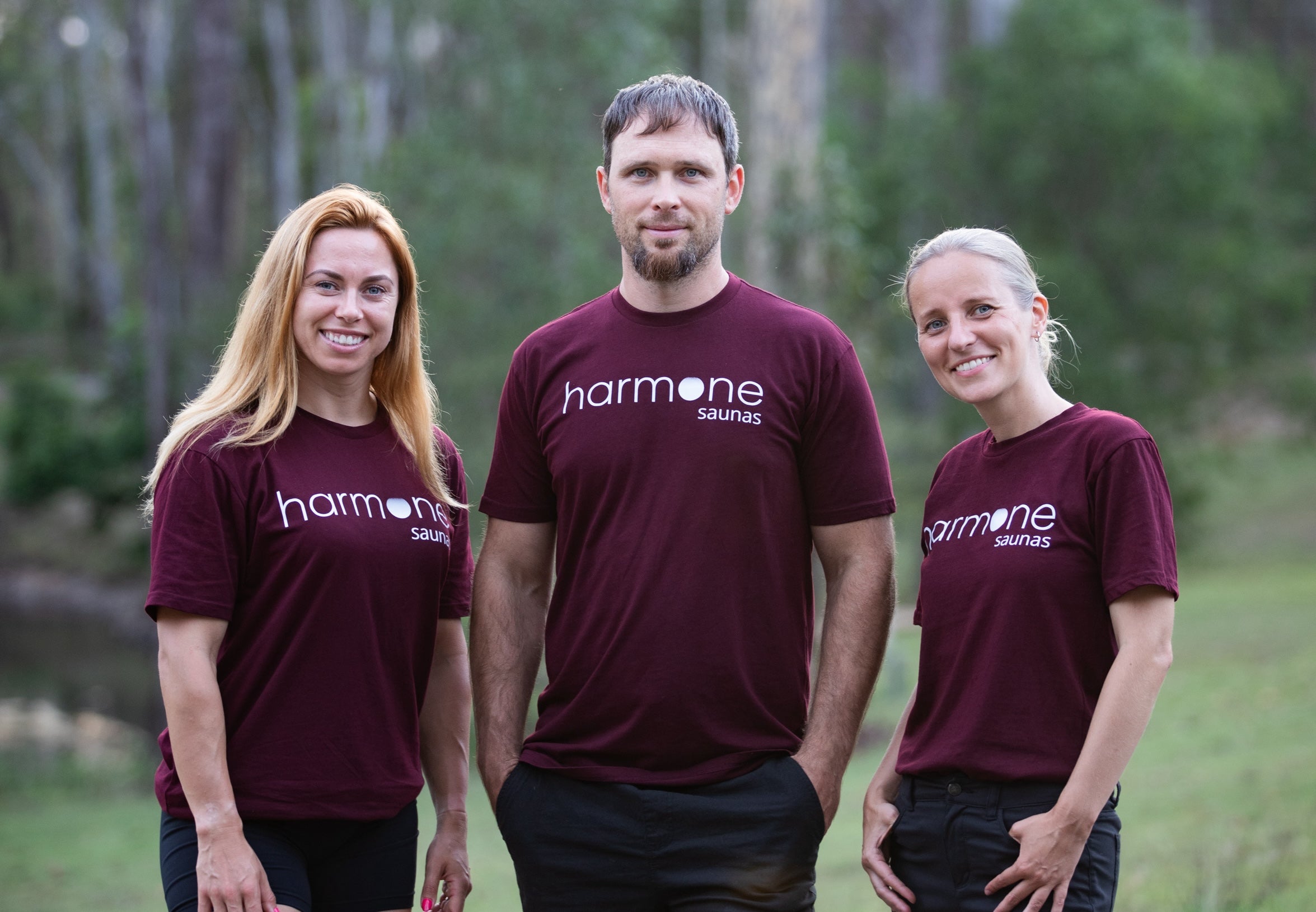 Three people wearing maroon 'harmone sauvé' t-shirts standing outdoors with a blurred natural background.