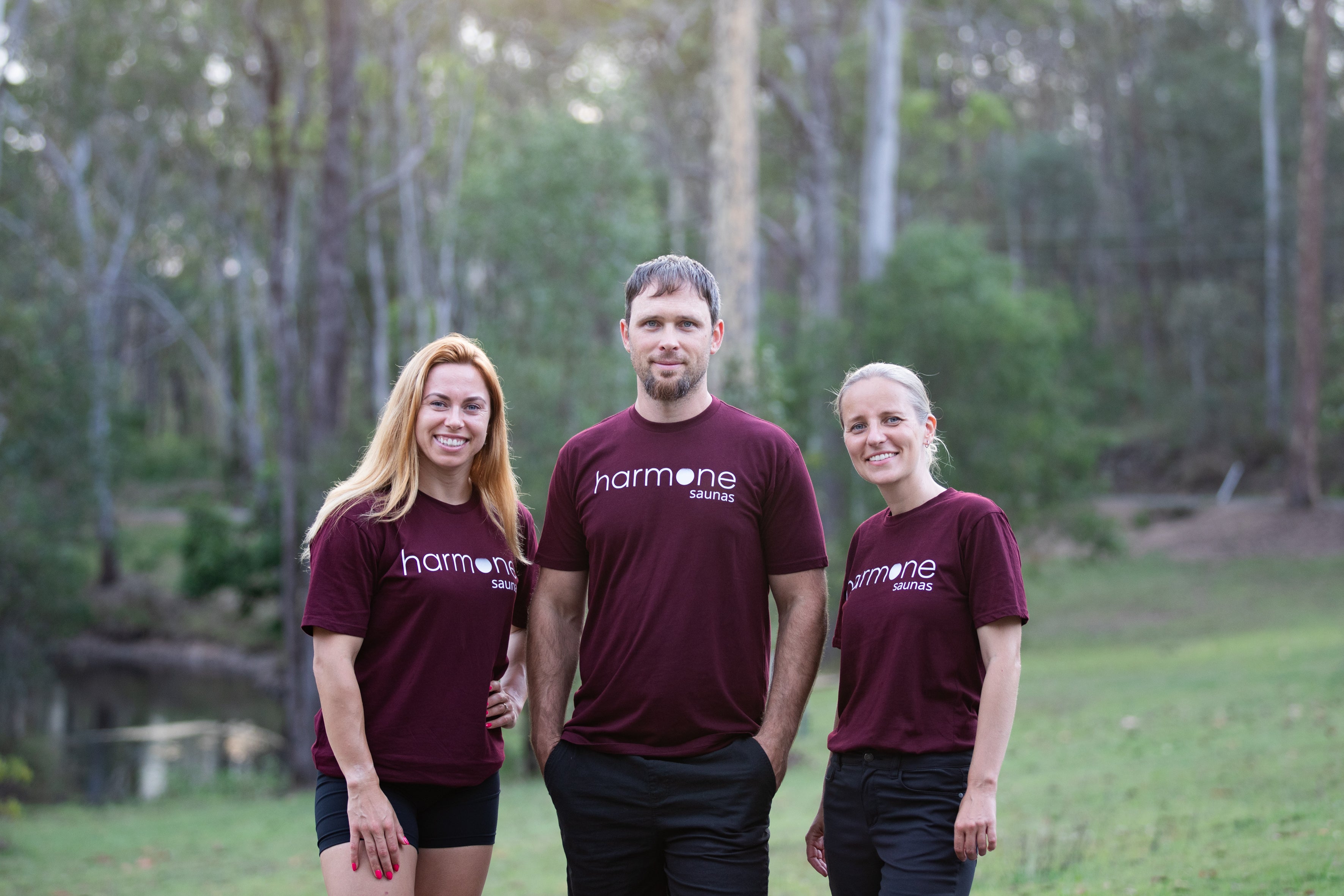 Three people wearing maroon 'hormone' shirts standing outdoors with trees in the background