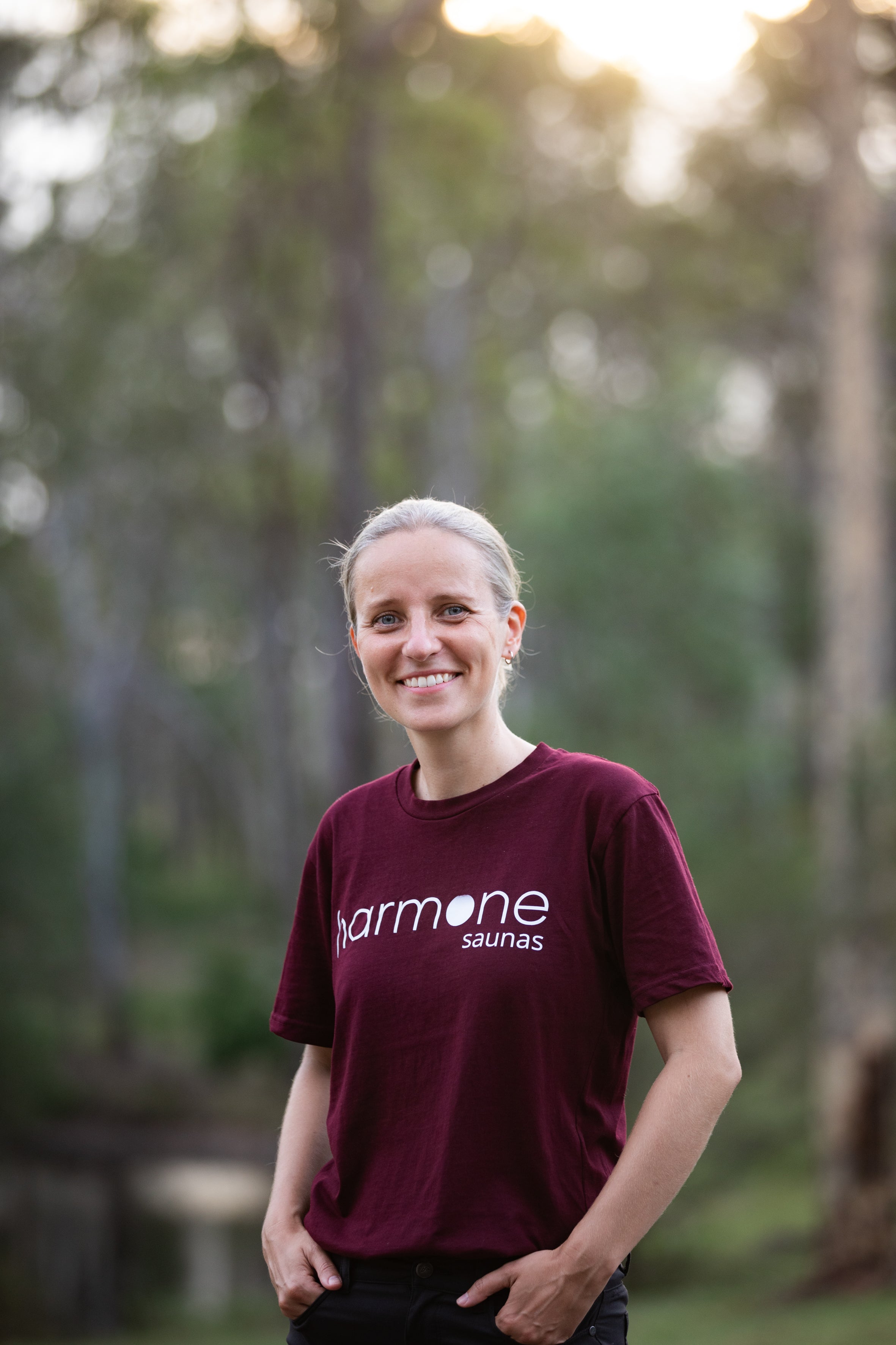 Person wearing a maroon t-shirt with 'harmone saunas' logo in a forest setting