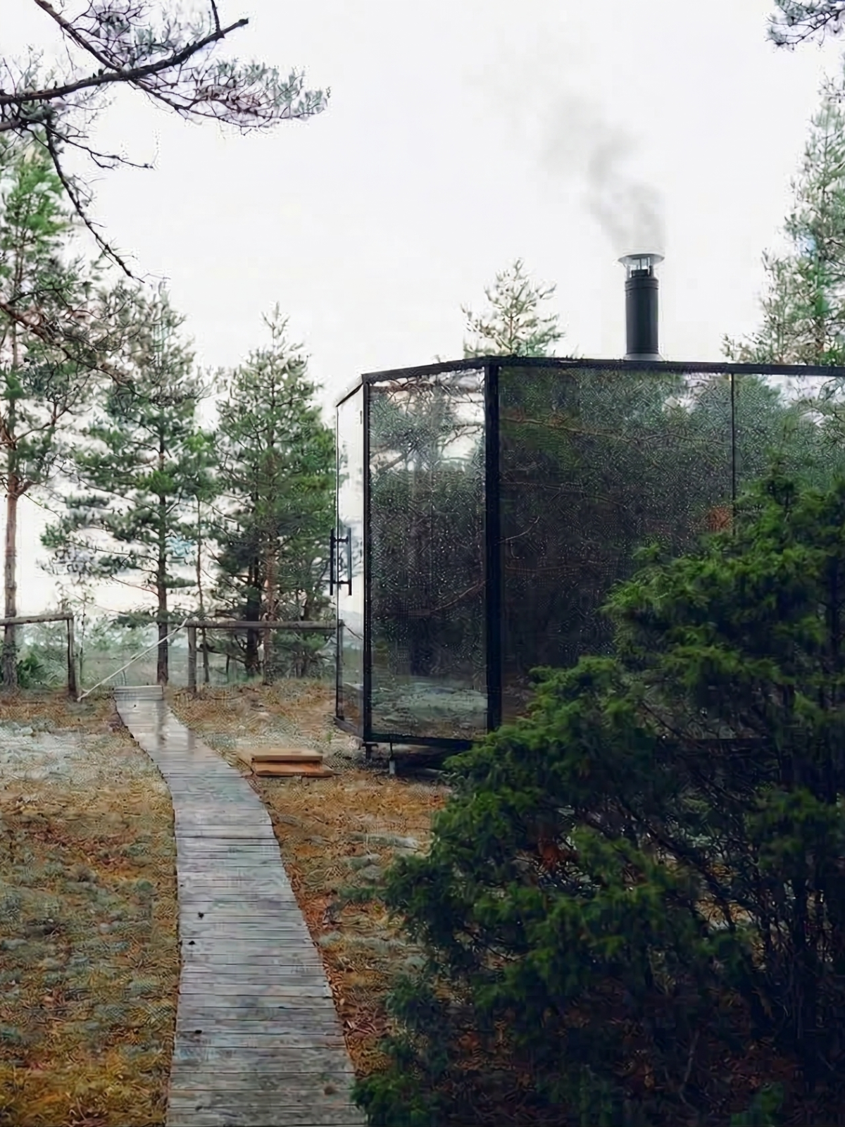 Wooden cabin in a forest with a smokestack emitting smoke.