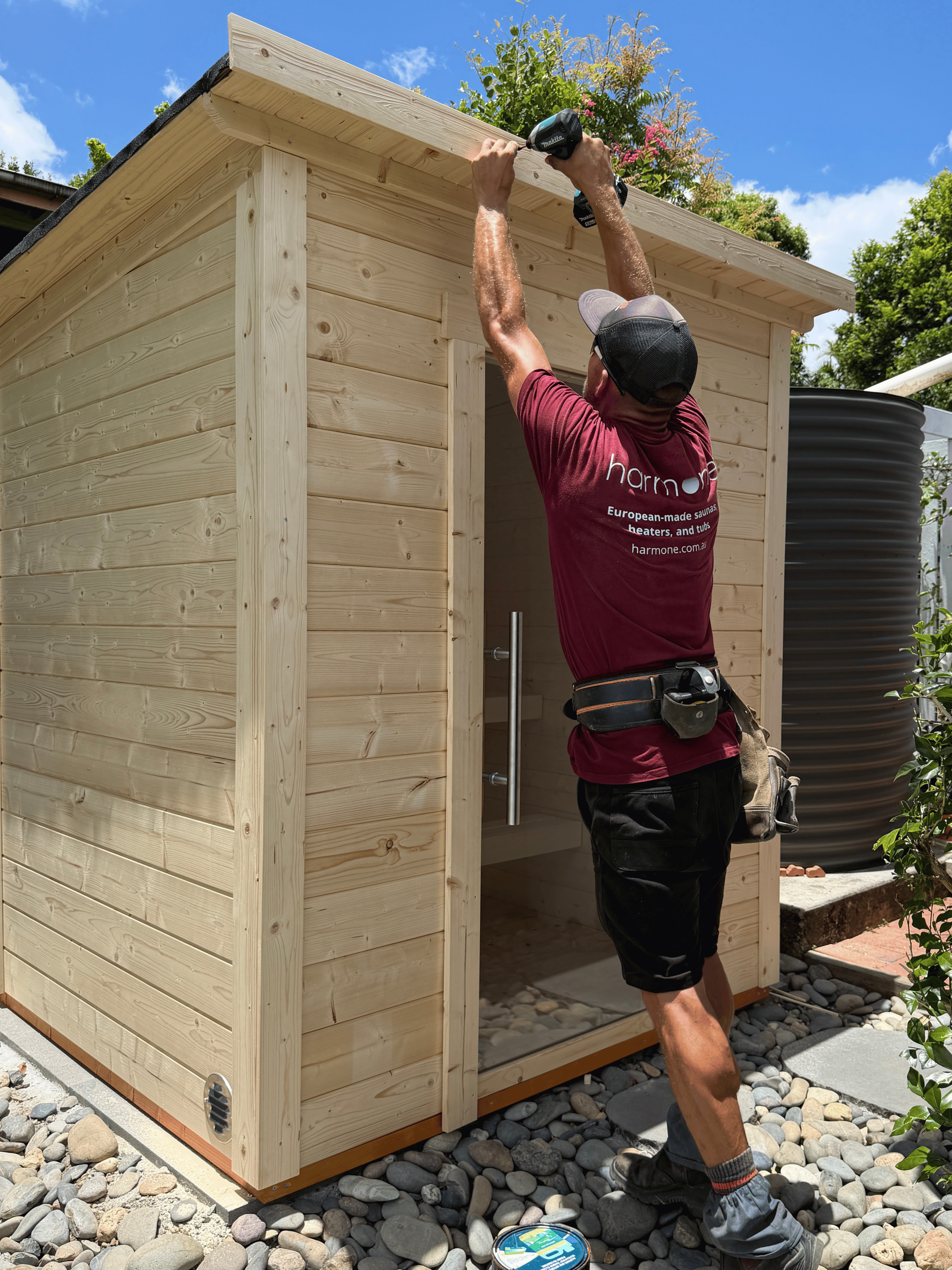 Person installing a wooden shed with tools, wearing a branded shirt.