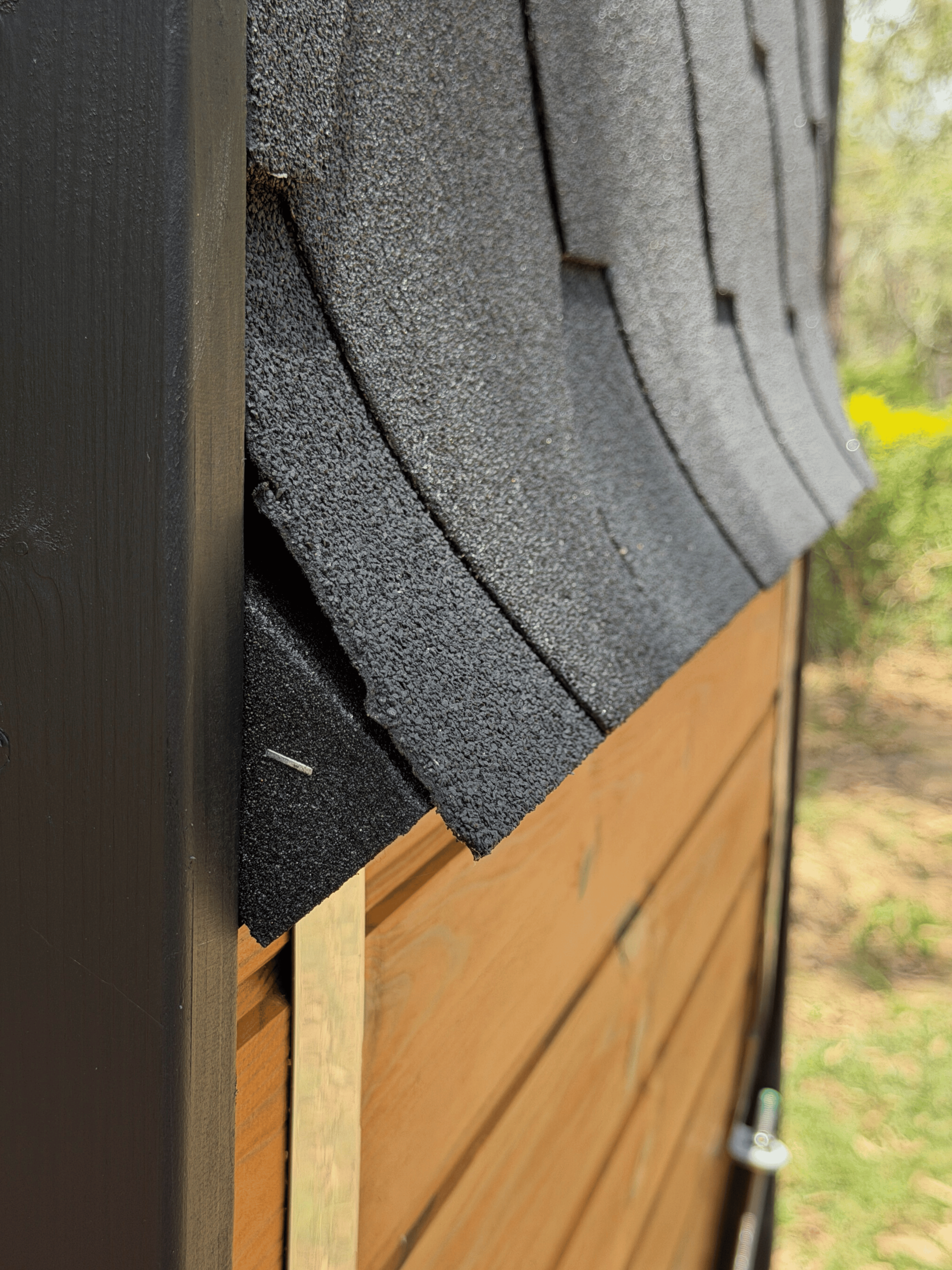 Close-up of a roof with gray shingles and wooden siding.