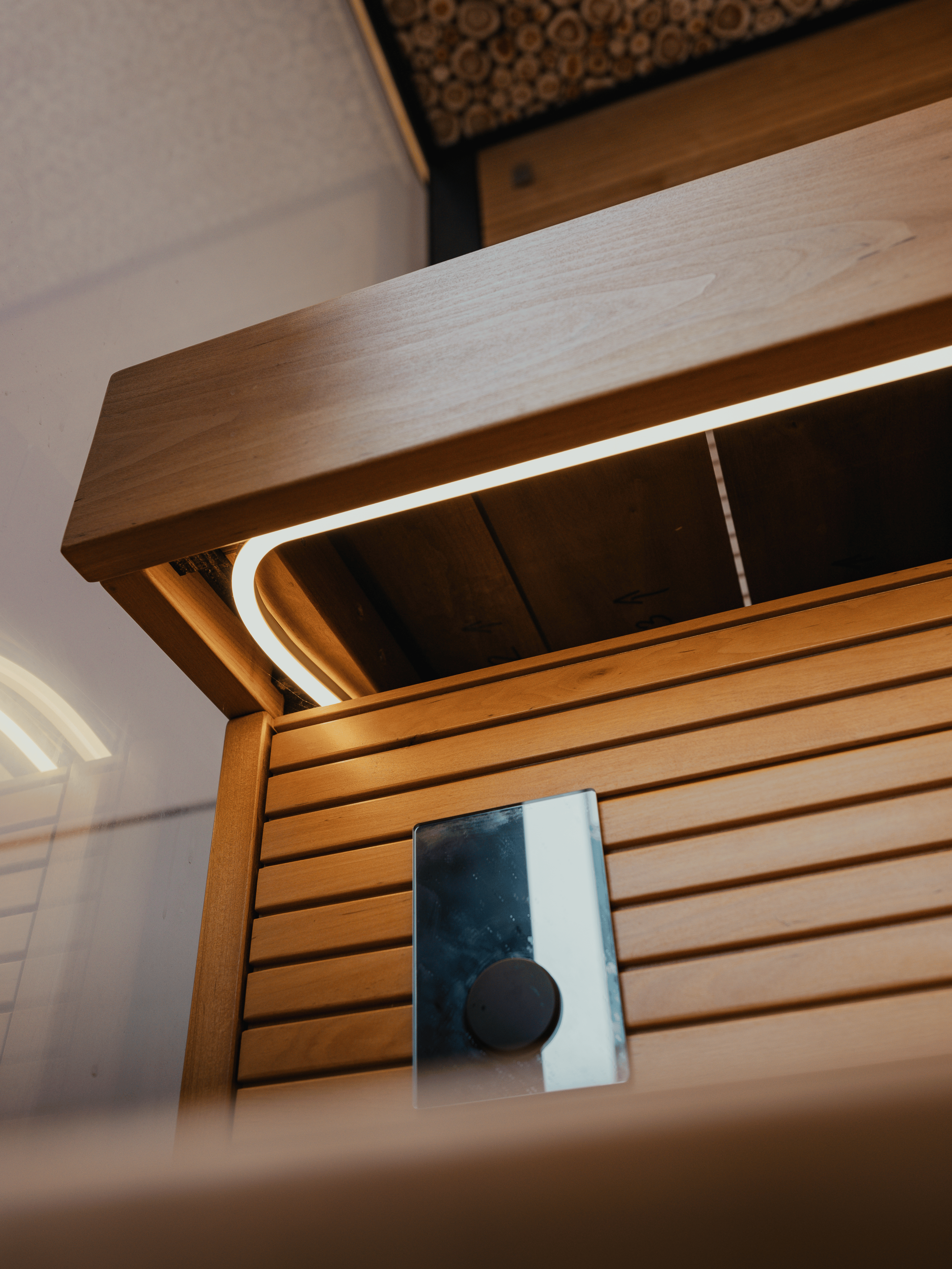 Wooden sauna bench with a mirror and light fixture inside a sauna.