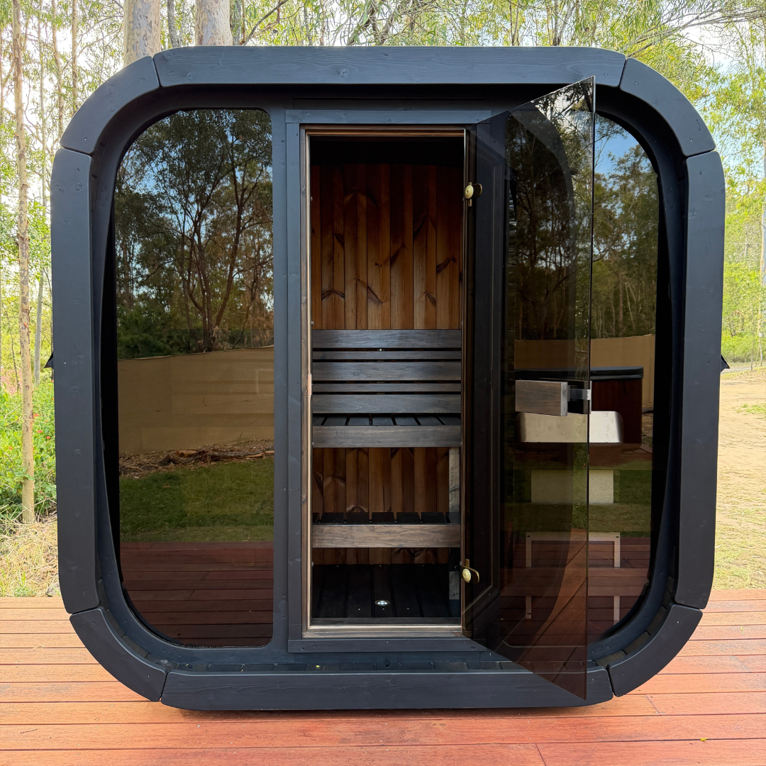 Portable sauna with black exterior and glass doors on a wooden deck.